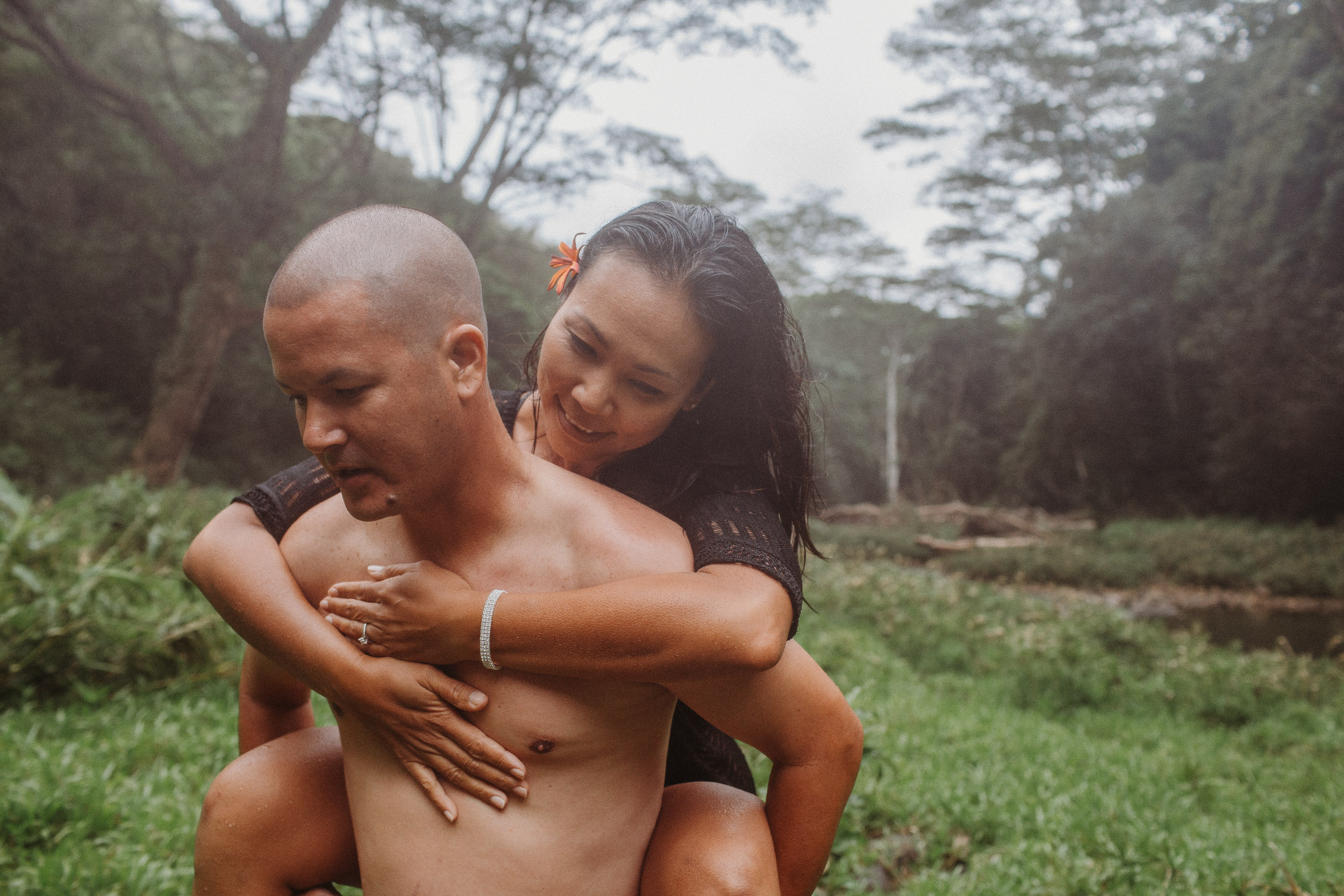 Man gives his fiance a piggyback ride in the rain during their Hawaii engagement photoshoot by Liz Koston.