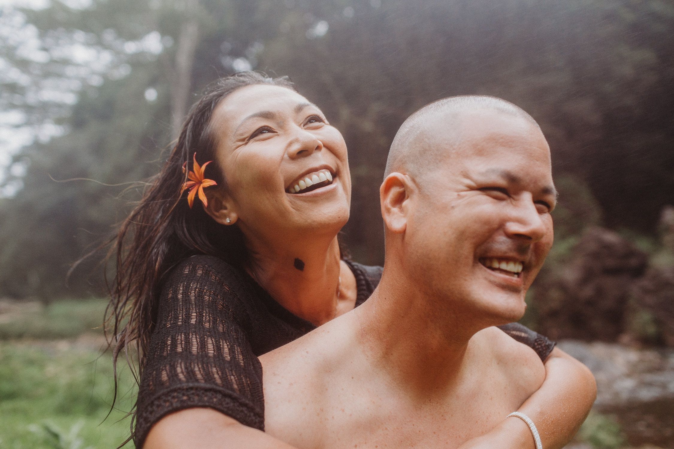 Woman goes for a piggyback ride on her fiance as they smile in the Hawaii rain during their Hawaii engagement photoshoot by Liz Koston.
