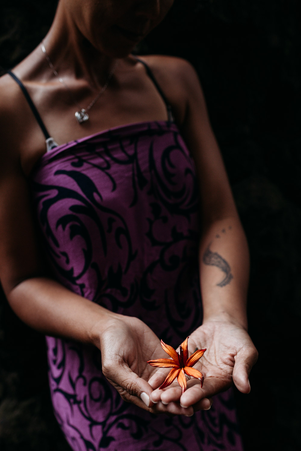 Woman holds bright orange flower in the palm of her hands during her Kauai photoshoot.