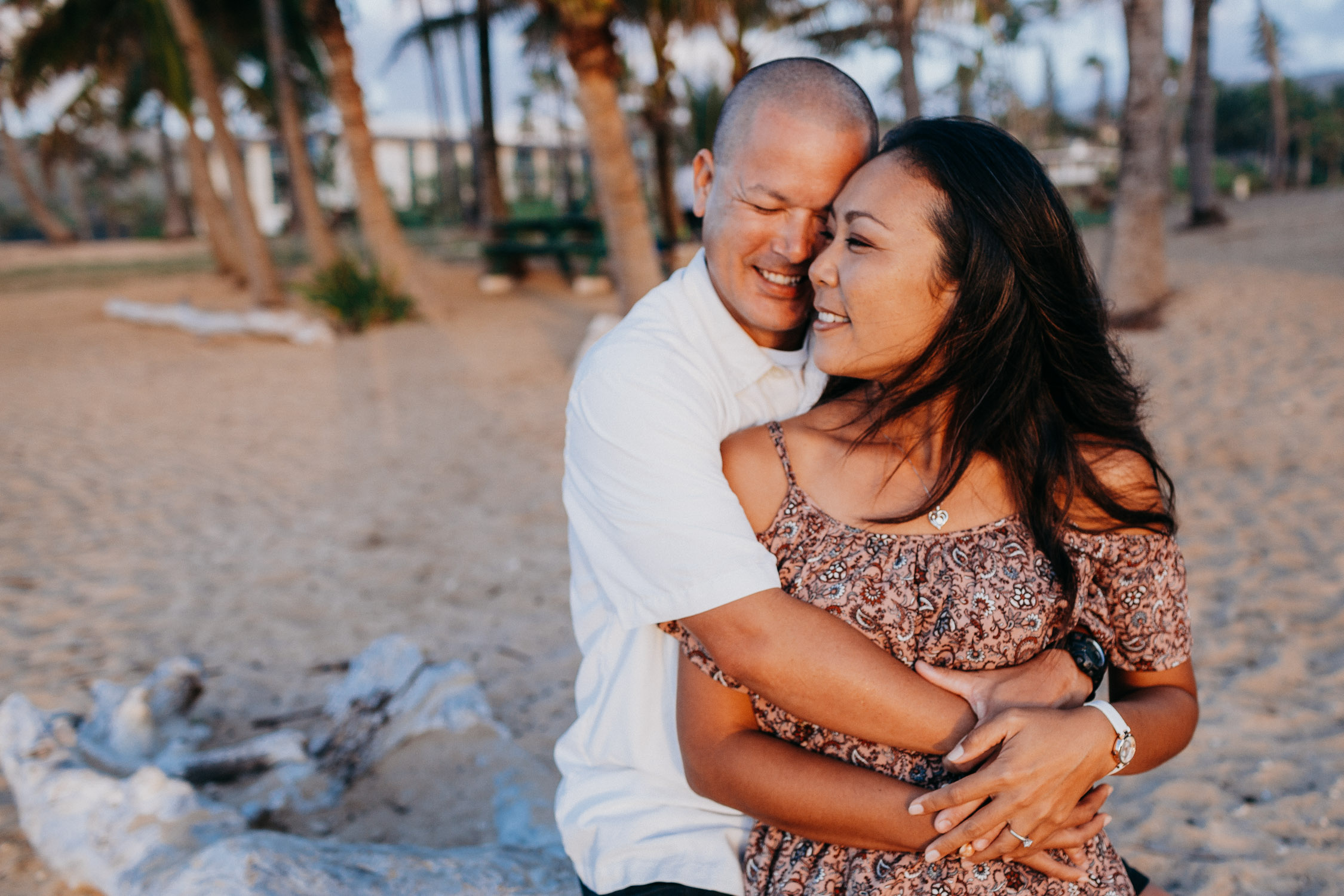Man hugs wife from behind while they both smile during their Hawaii beach photoshoot by Liz Koston. 