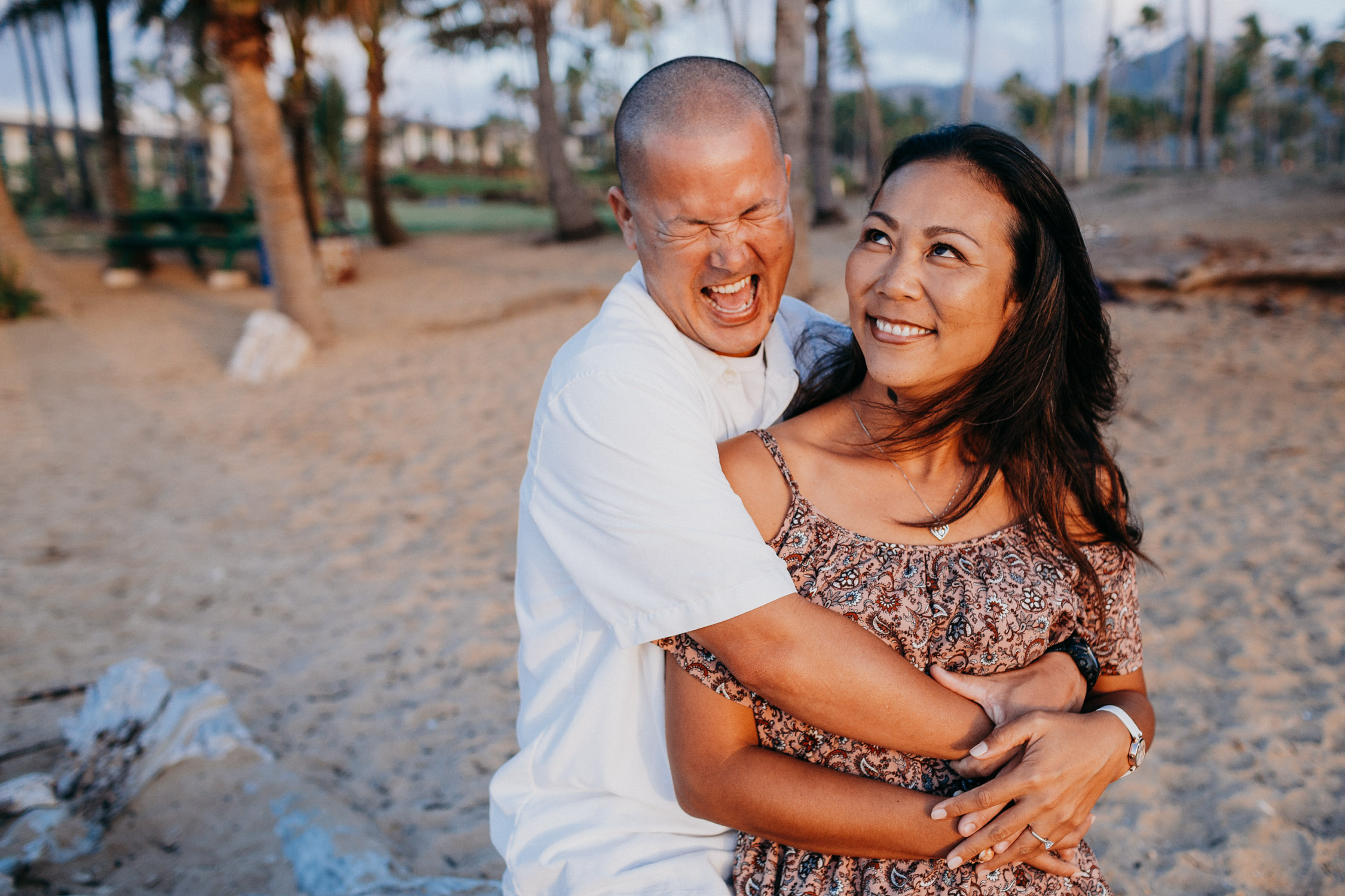 Husband hugs his wife from behind with a big smile during their anniversary photoshoot in Hawaii by Liz Koston.
