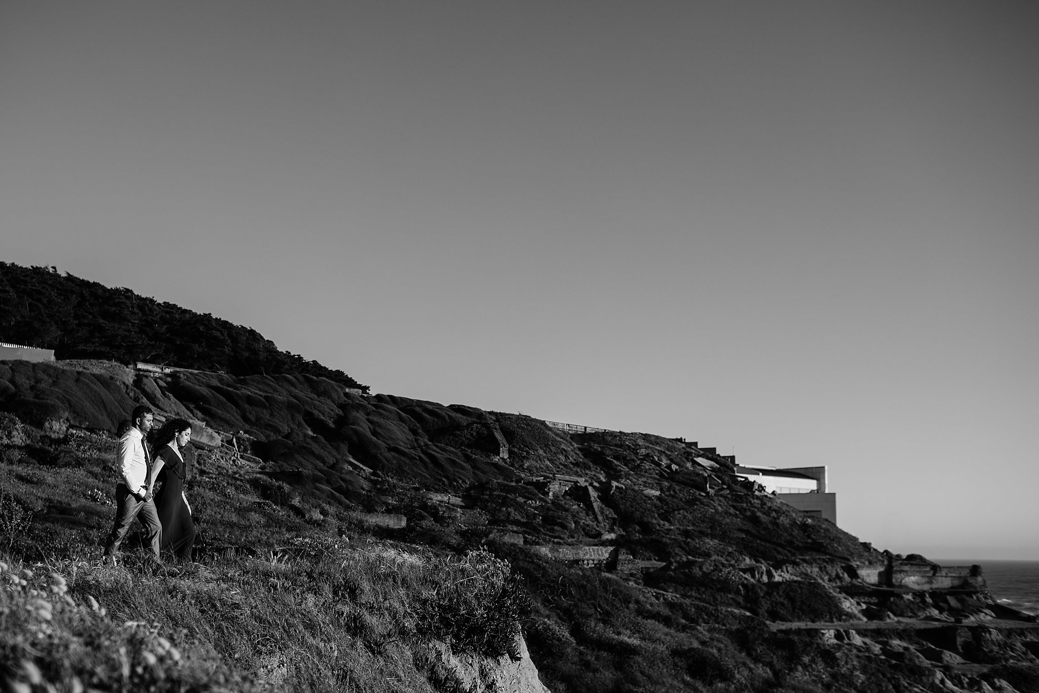 Black and white image of couple standing at the Sutro Baths overlook during their engagement photoshoot.