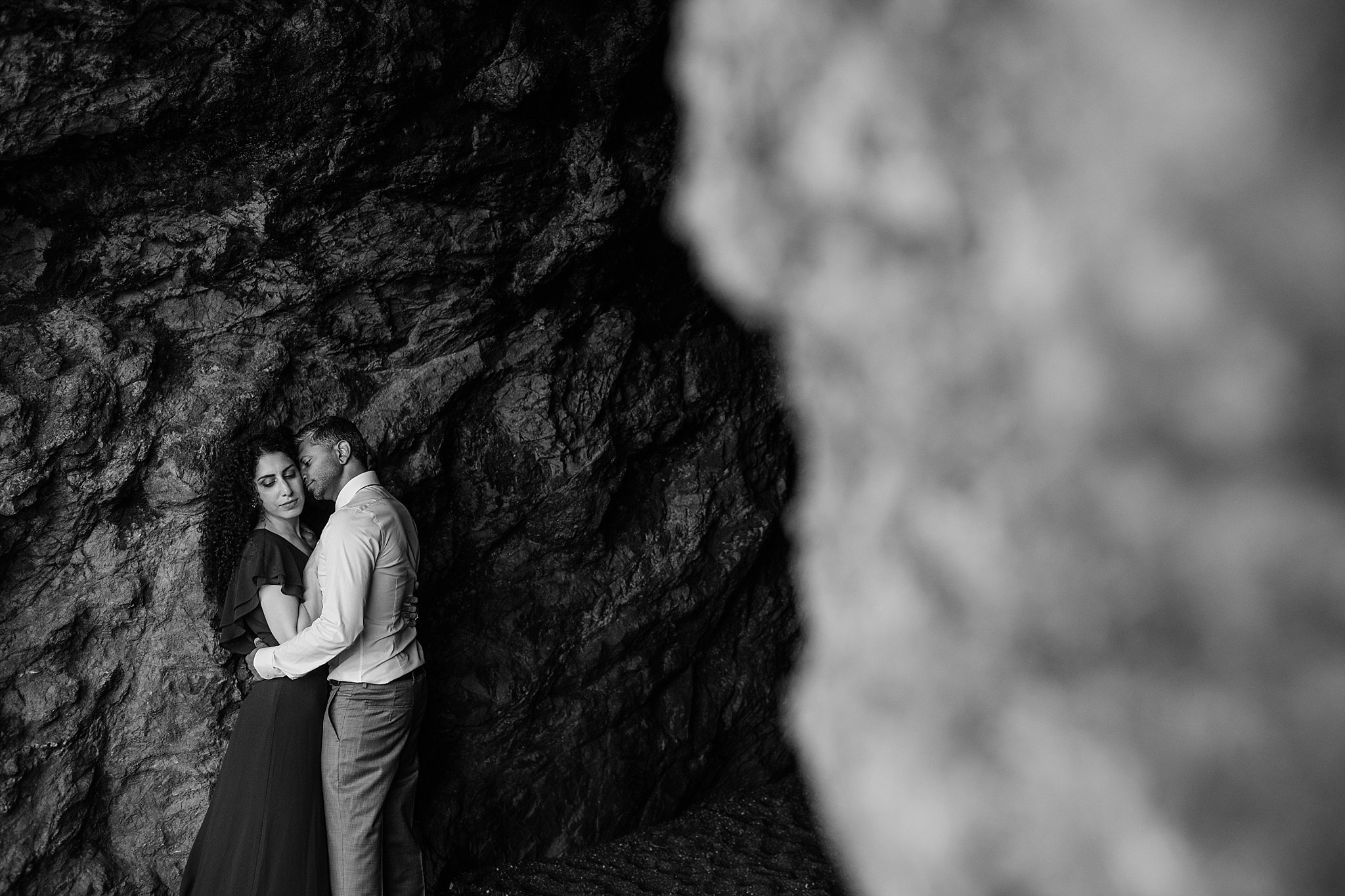 Black and white image of couple in a loving embrace against a rocky backdrop in San Francisco, CA