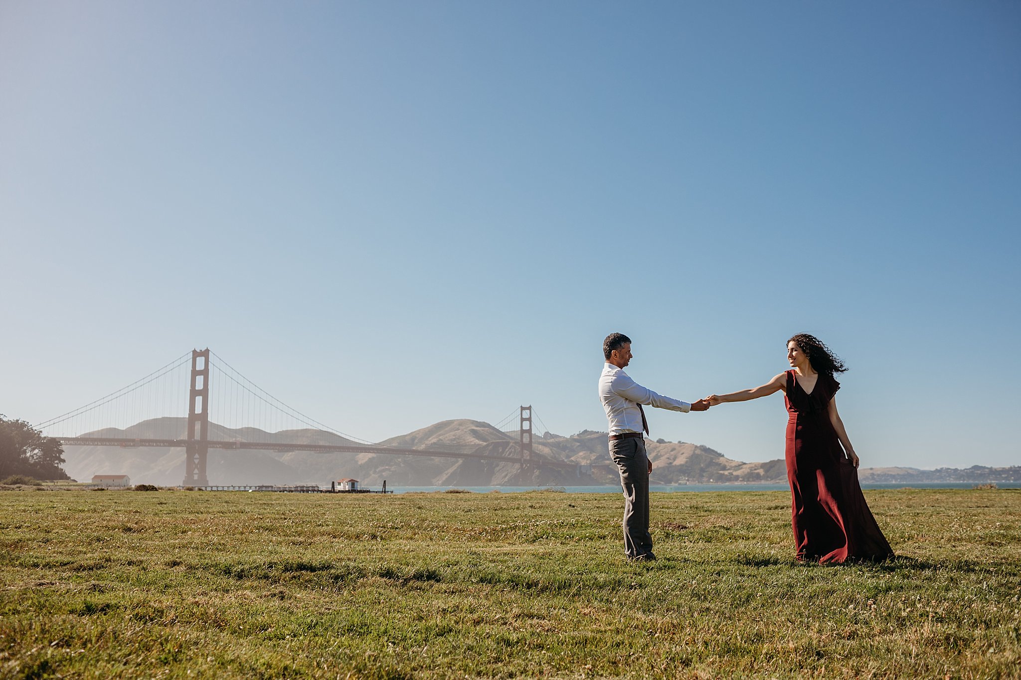 Couple holding hands at Chrissy Field with the Golden Gate Bridge in the background during their San Francisco engagement photoshoot.