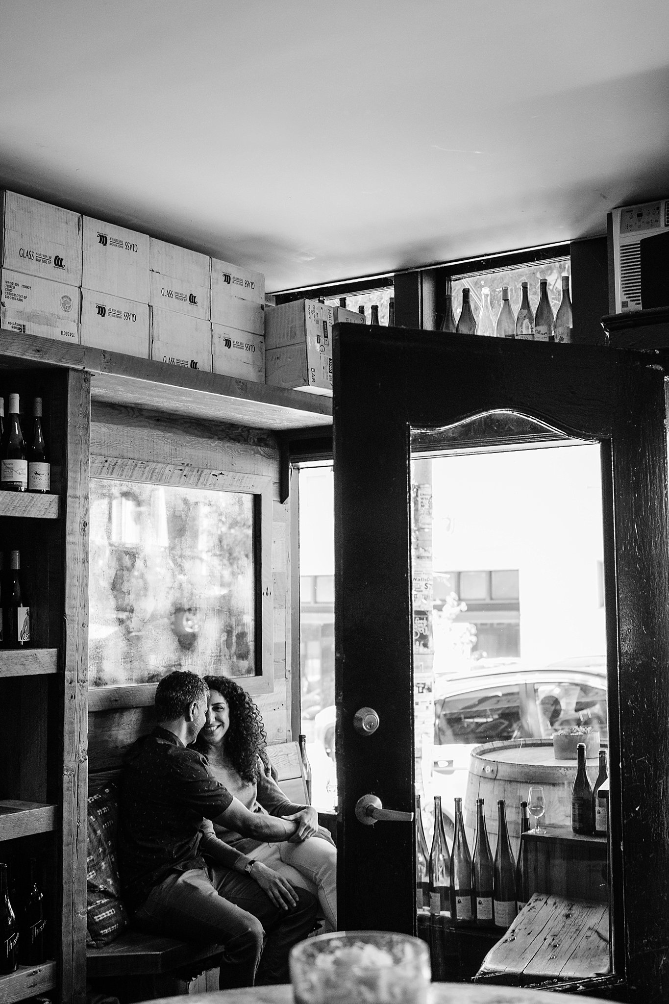 Couple sits in corner booth of wine store during their San Francisco engagement photoshoot