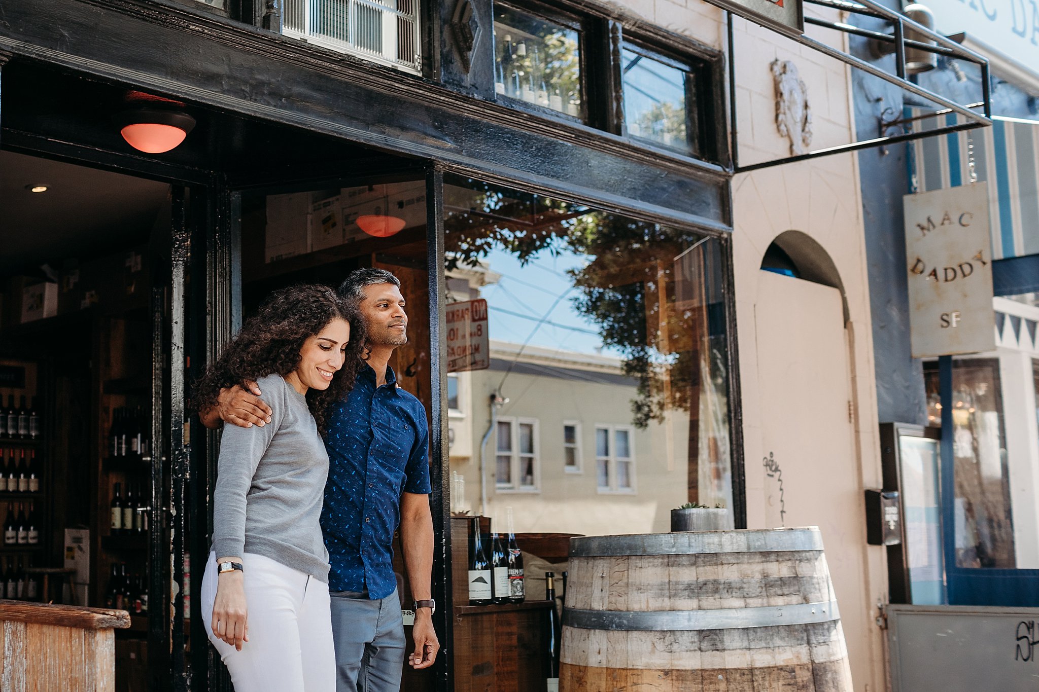 Couple stands arm in arm outside a wine shop in San Francisco during their engagement photoshoot.