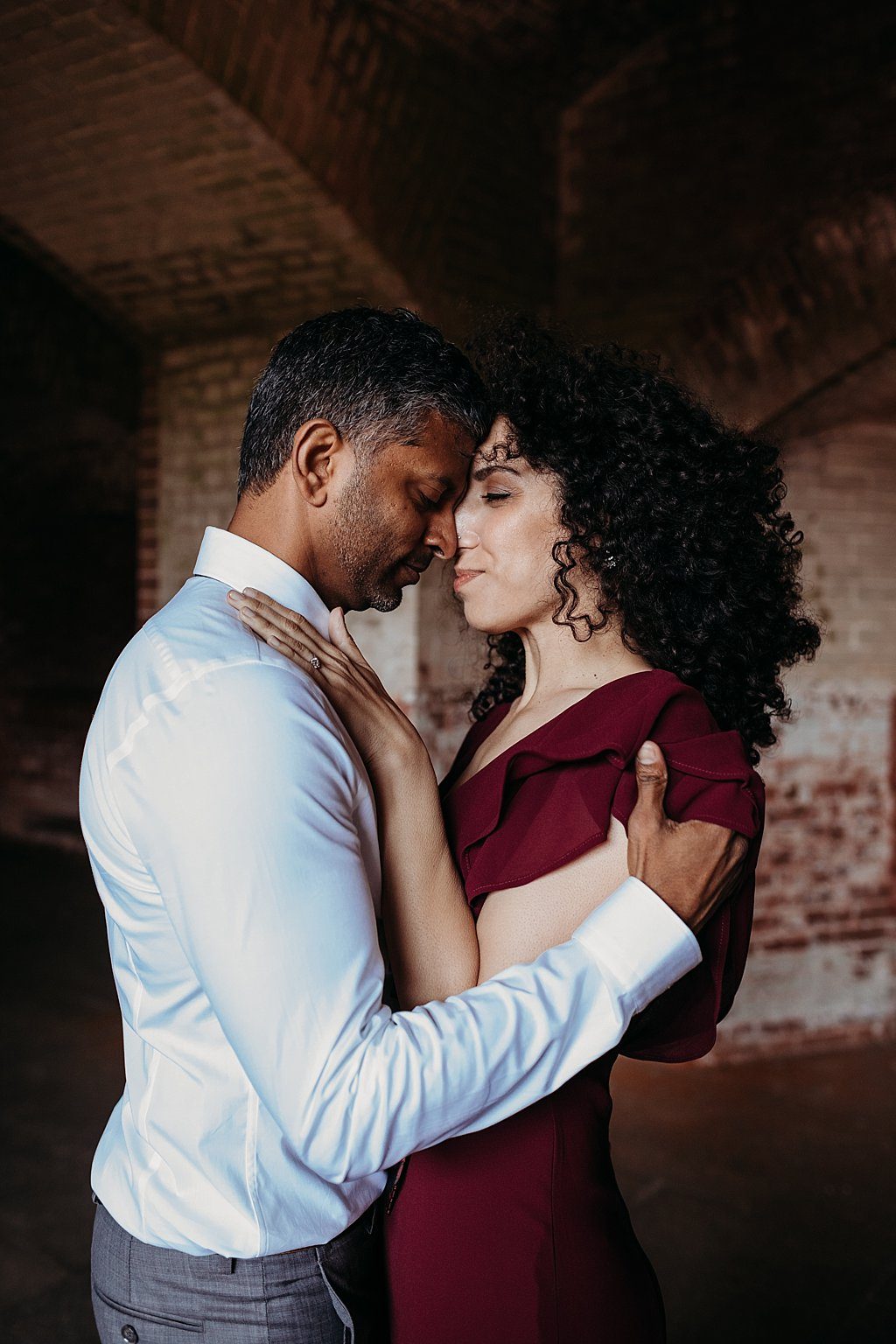 Couple stands with foreheads touching in an embrace during their Fort Point engagement photoshoot in San Francisco, CA
