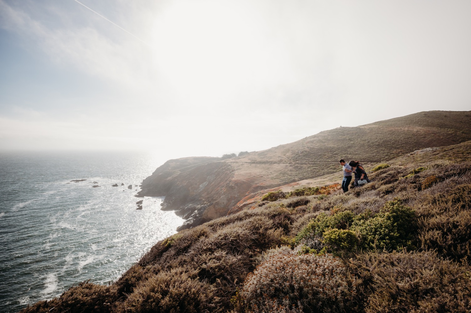 Couple walks on bluff over the Pacific Ocean during their Rodeo Beach engagement photoshoot.