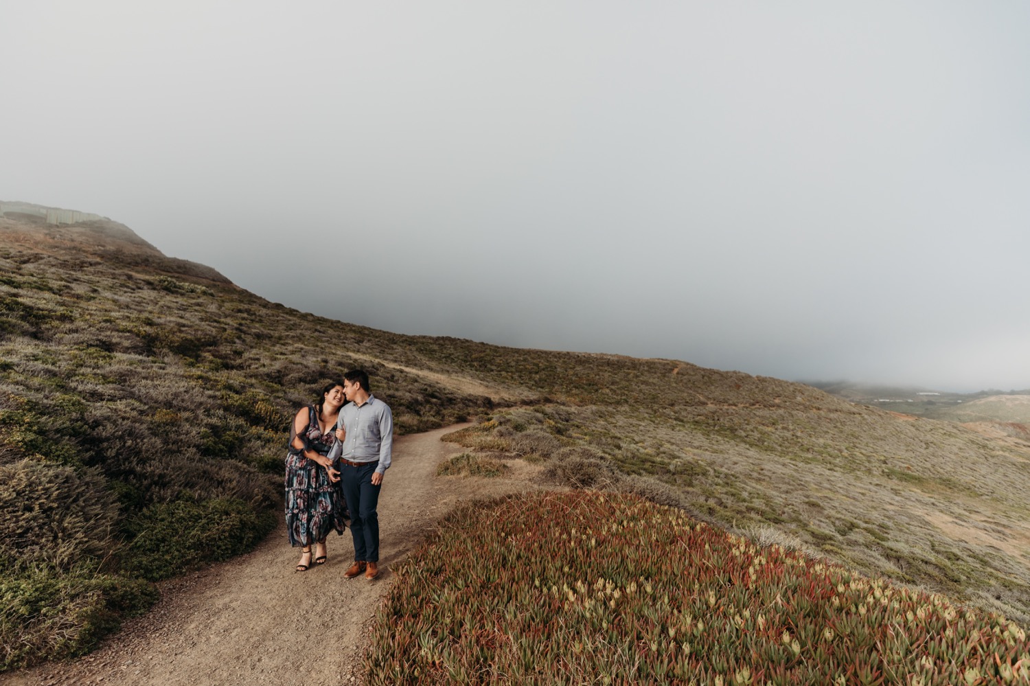 Couple walks along a coastal trail near Rodeo Beach the woman gazes lovingly up at her fiance.