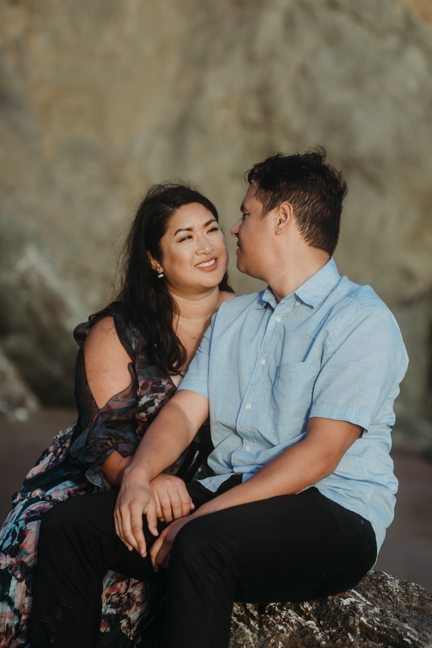 Couple sit on a rock gazing at each other during their Rodeo Beach engagement photoshoot.