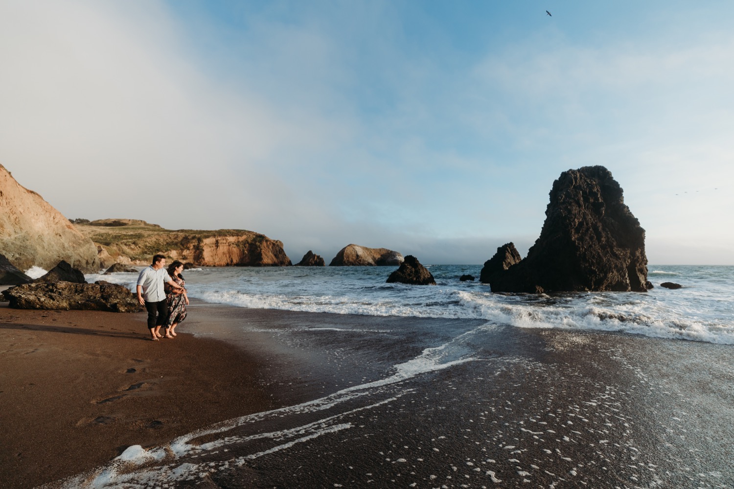 Couple walks along the rock stacks at Rodeo Beach during their sunset engagement photoshoot.