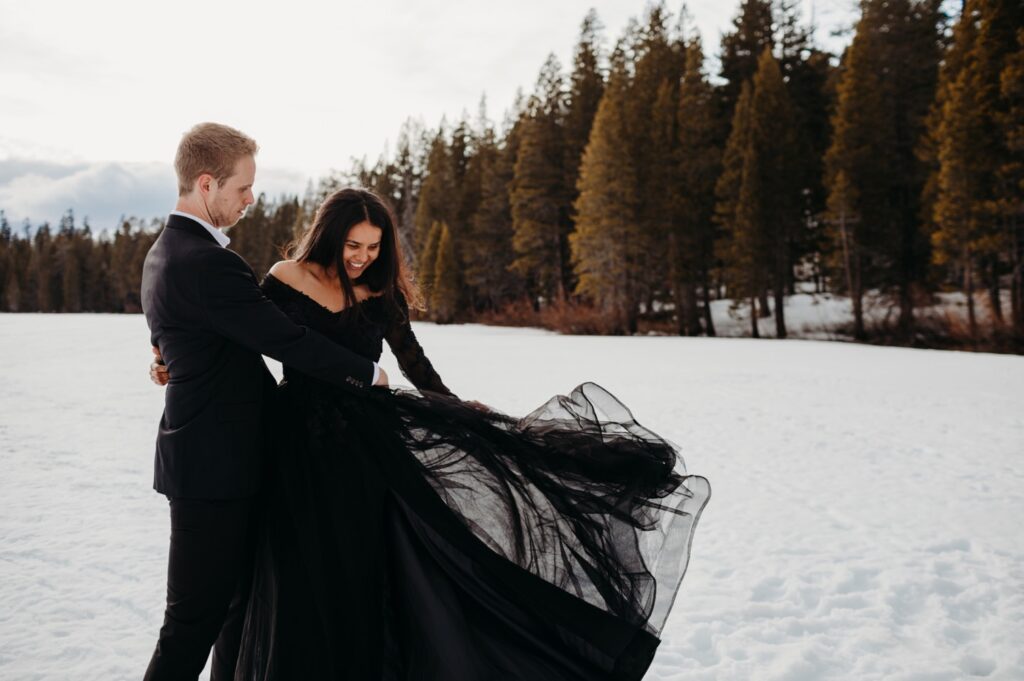 Couples in all black outfits against the snow. dancing lifting in meadow full of snow