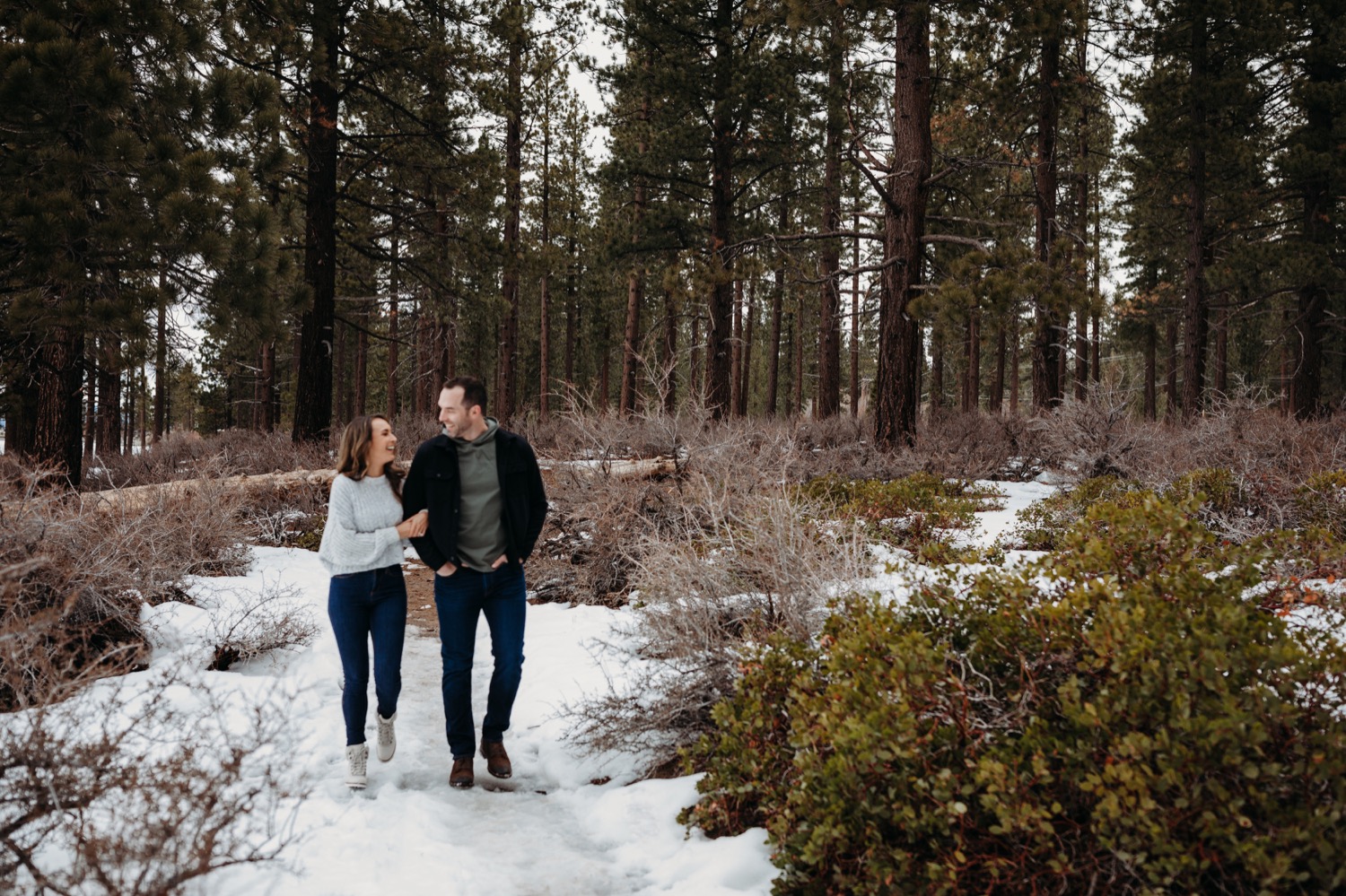 Zephyr-Cove-Winter-Engagement-Session. couple walking together in the trees with snow on the ground while looking at each other