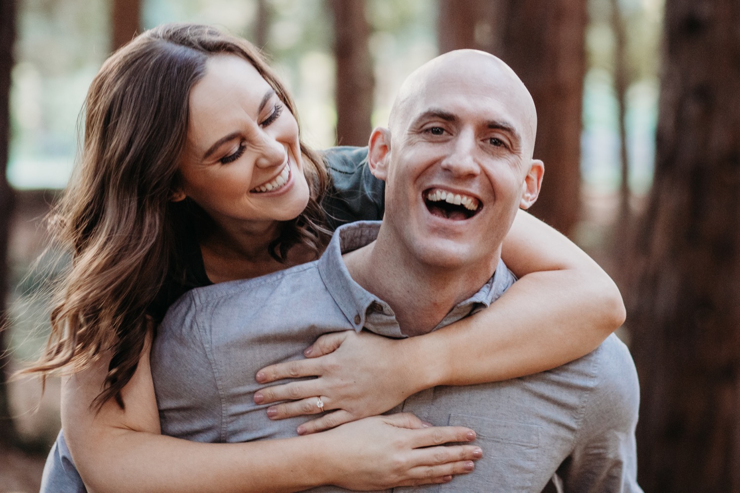 Woman goes on piggyback ride while smiling at her smiling fiance on their Golden Gate Park engagement photoshoot.