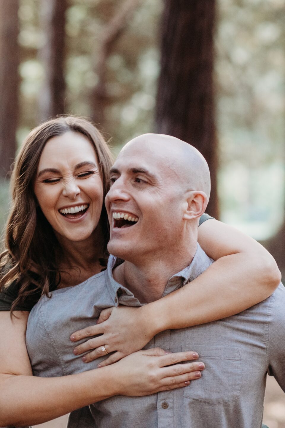 Woman goes on piggyback ride while smiling at her smiling fiance on their Golden Gate Park engagement photoshoot.