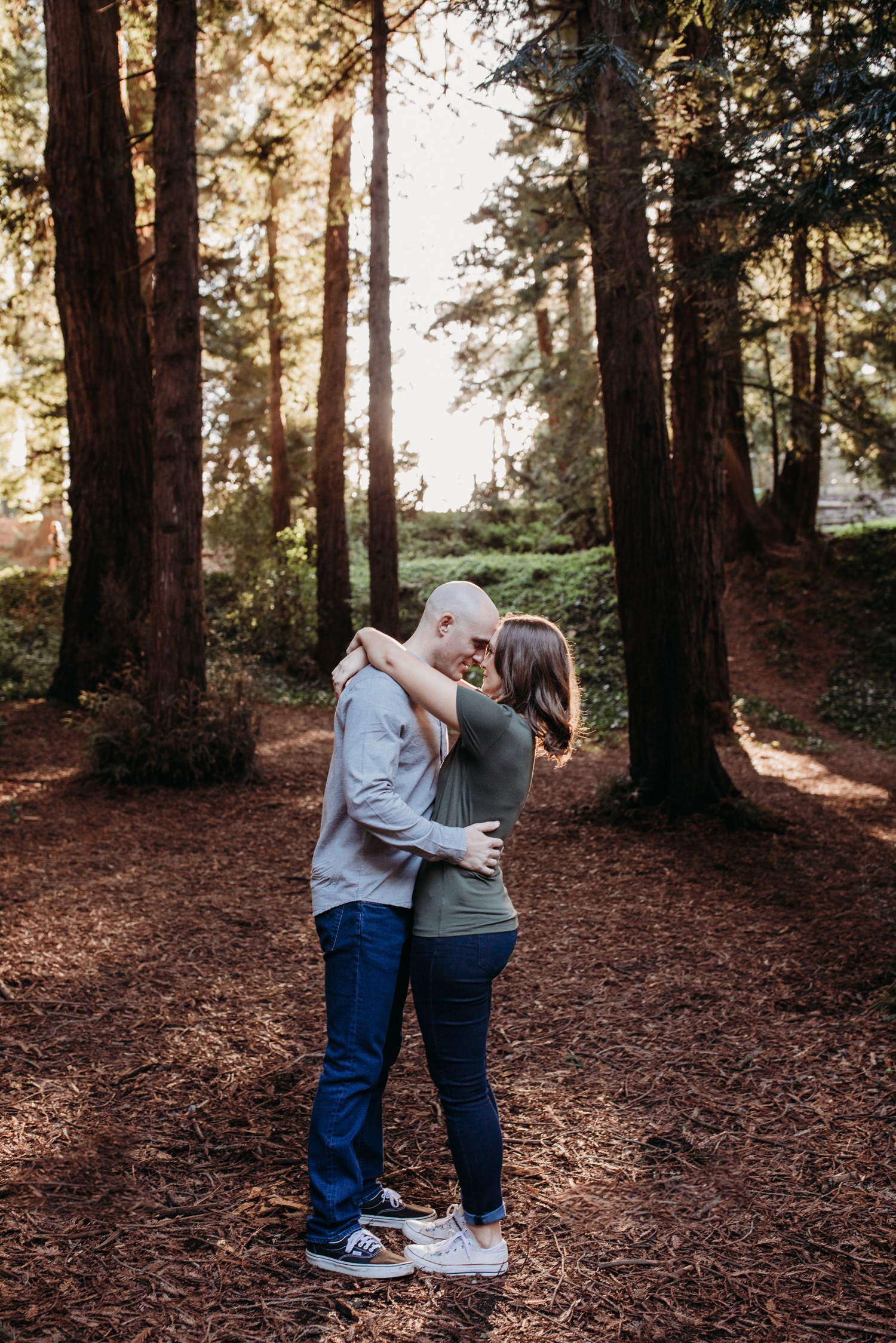 Couple hugs while touching foreheads in the middle of the Golden Gate Park redwoods on their San Francisco engagement photoshoot.