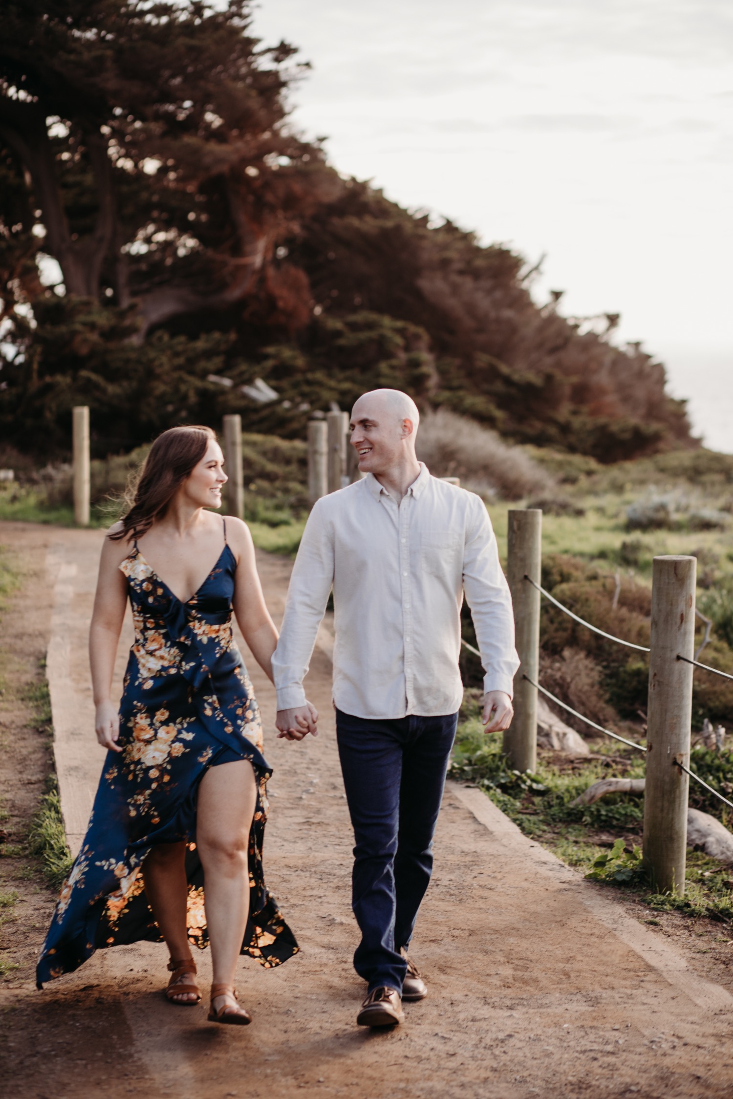 Couple walks holding hands down a dirt path on their Sutro Baths engagement photoshoot.