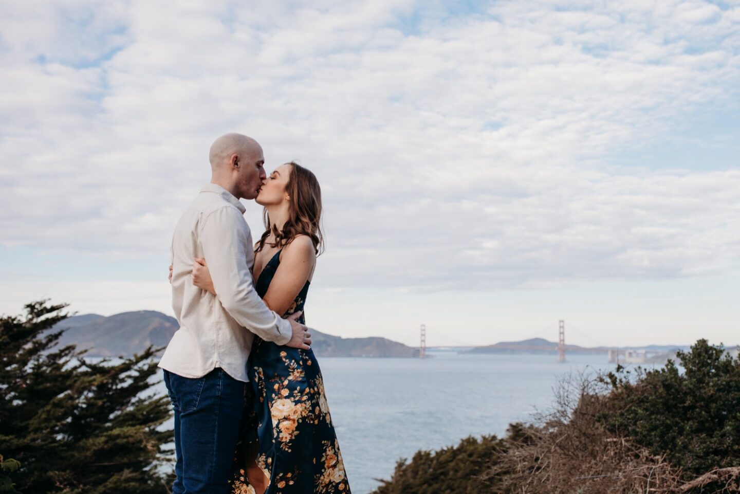 Couple kisses with a view of the Golden Gate Bridge in the background during their Sutro Baths engagement photoshoot.