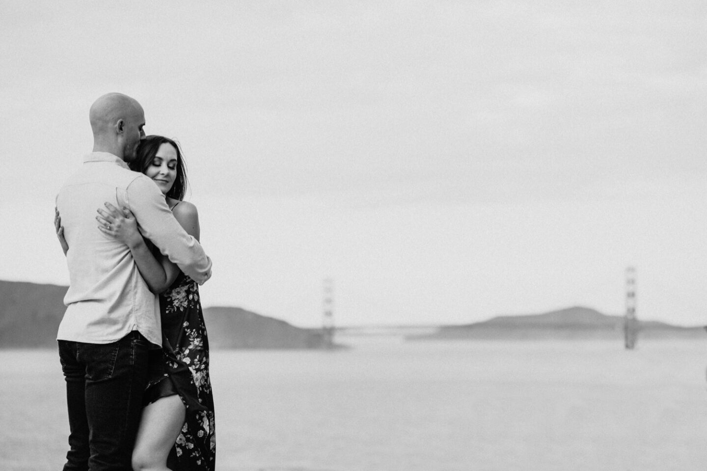 Couple hugs with a view of the Golden Gate Bridge on their San Francisco engagement photoshoot.