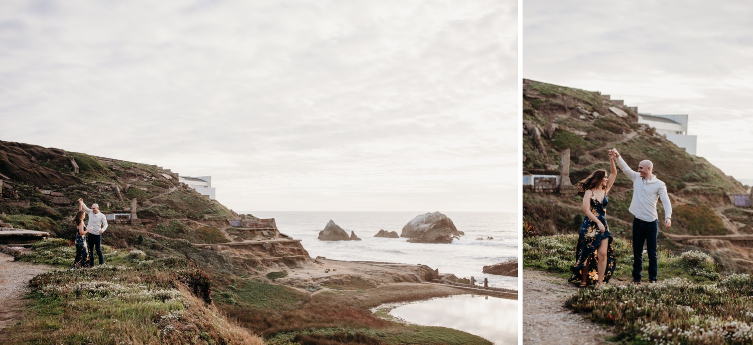 Man spins his fiance with a view of Sutro Baths in the distance on their engagement photoshoot.