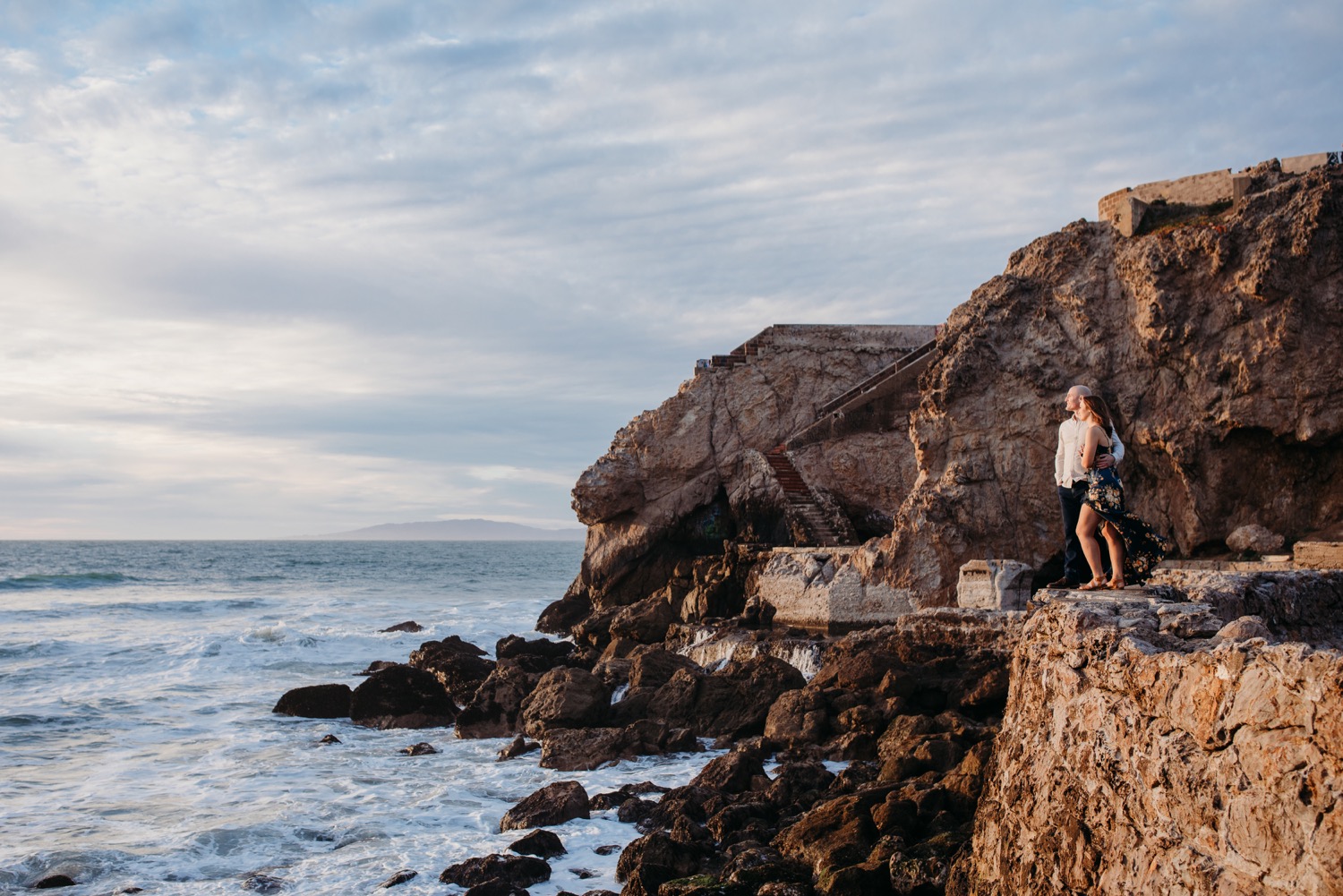 Couple gazes out over the Pacific Ocean during their sunset engagement photoshoot at Sutro Baths.