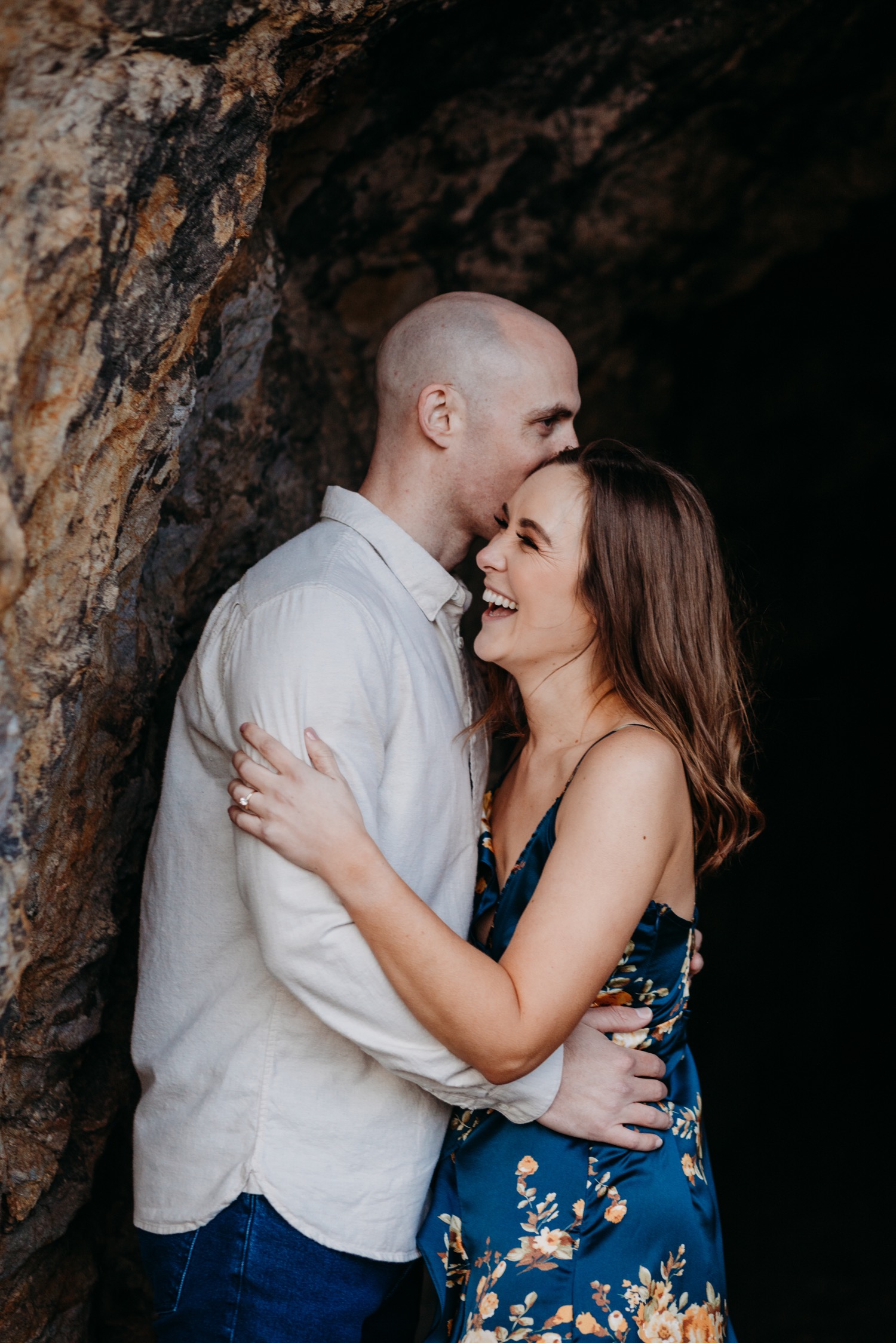 Man whispers in his fiance's ear during their Sutro Baths engagement photos.