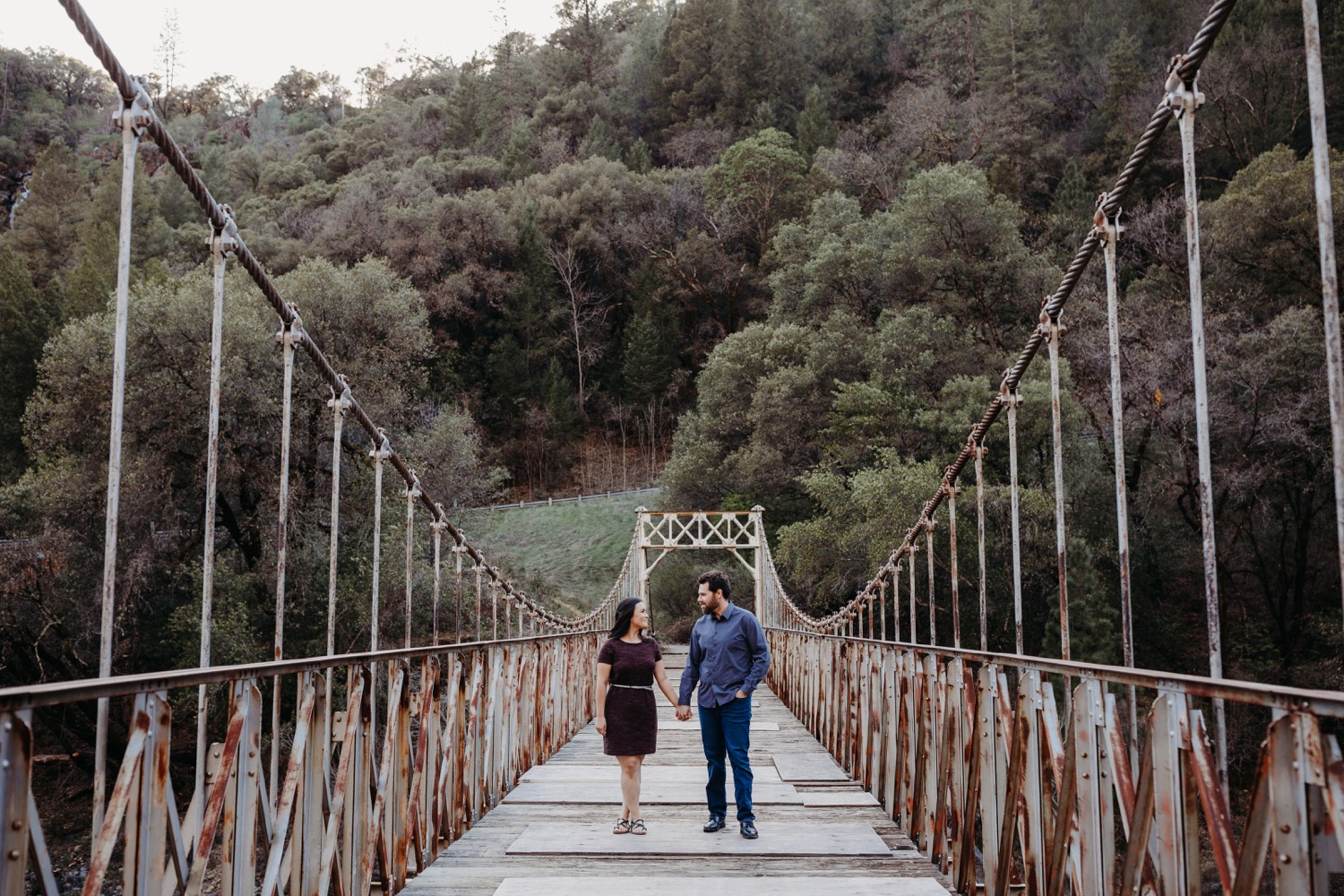 Couple walks down a suspension bridge holding hands on their Sacramento engagement photoshoot.