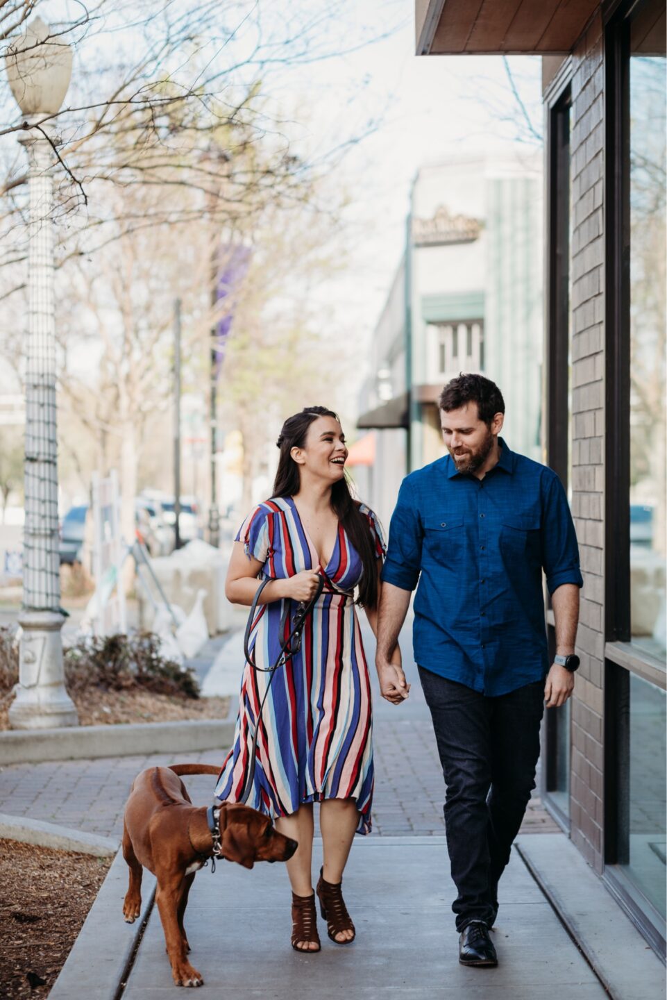 Couple walks down the street holding hands with their dog on their Davis engagement photoshoot.
