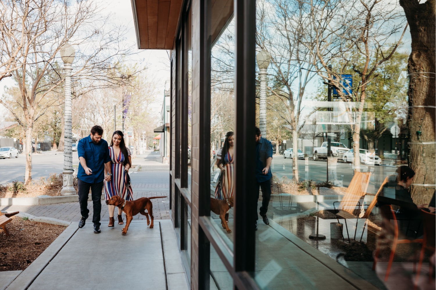 Couple walks with dog down a city street during their Davis engagement photoshoot.