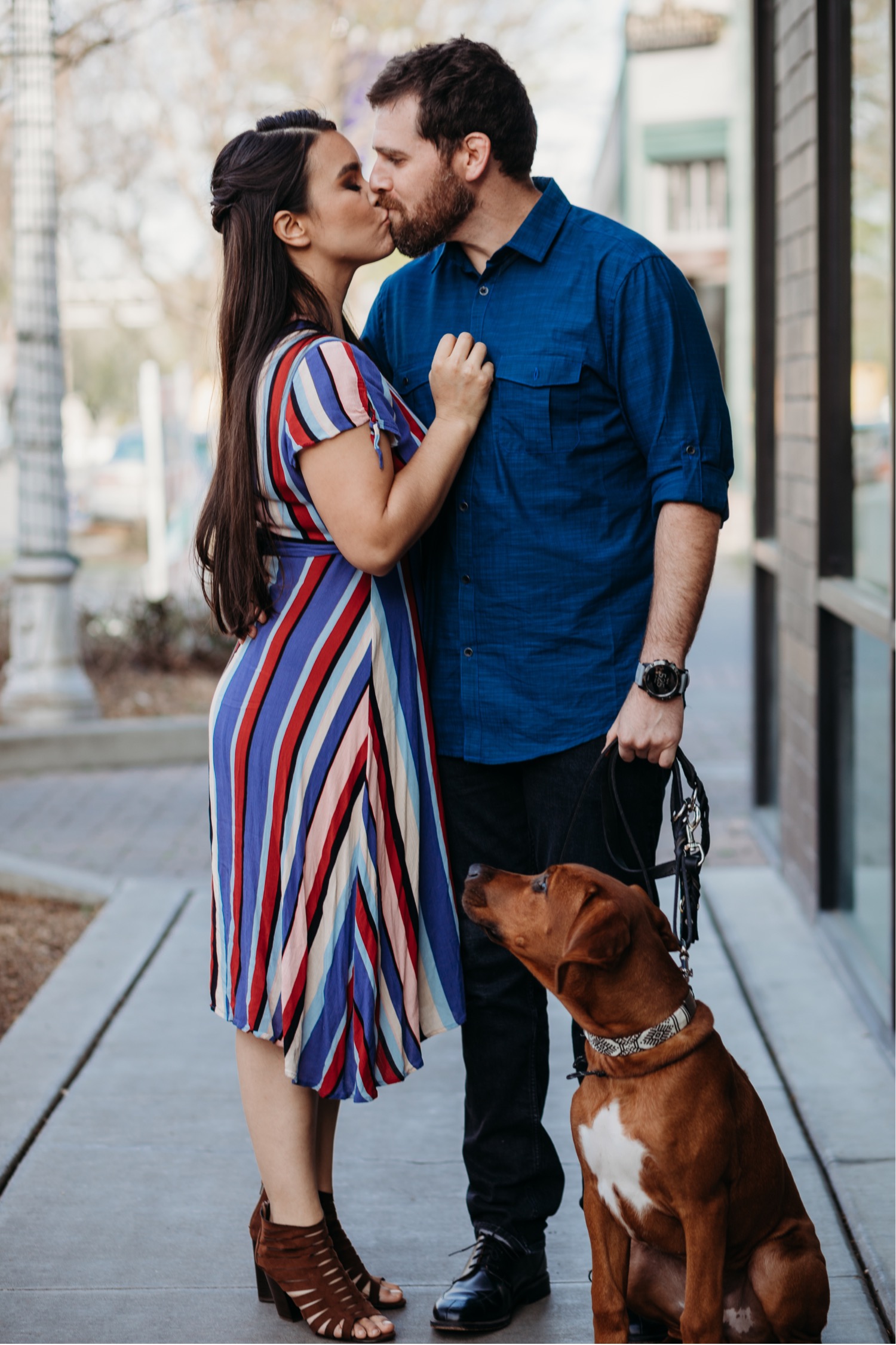 Couple kisses while their cute brown dog looks up at them during their Downtown Davis engagement photoshoot.