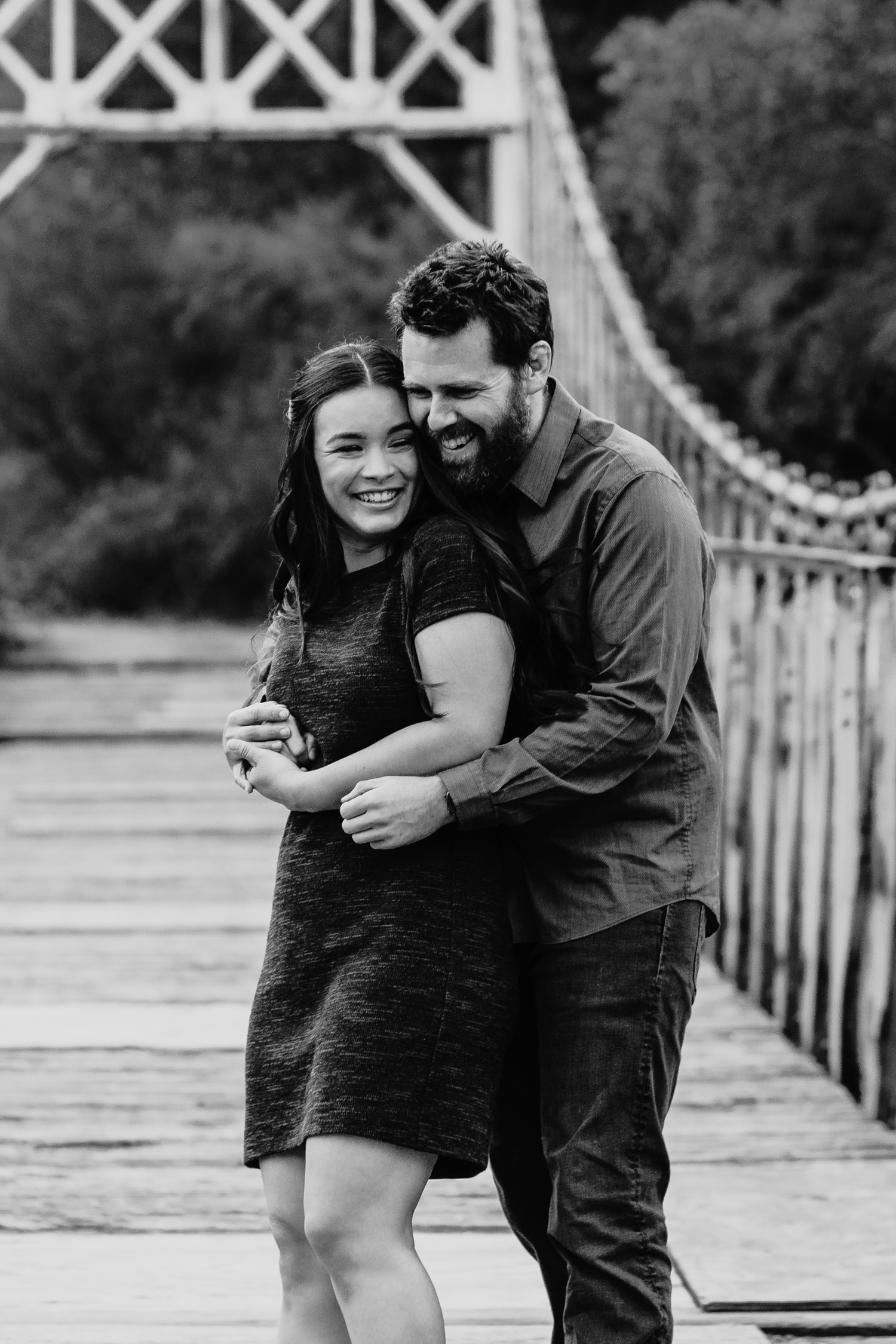Man hugs his fiance from behind on a suspension bridge during their Sacramento engagement photoshoot.