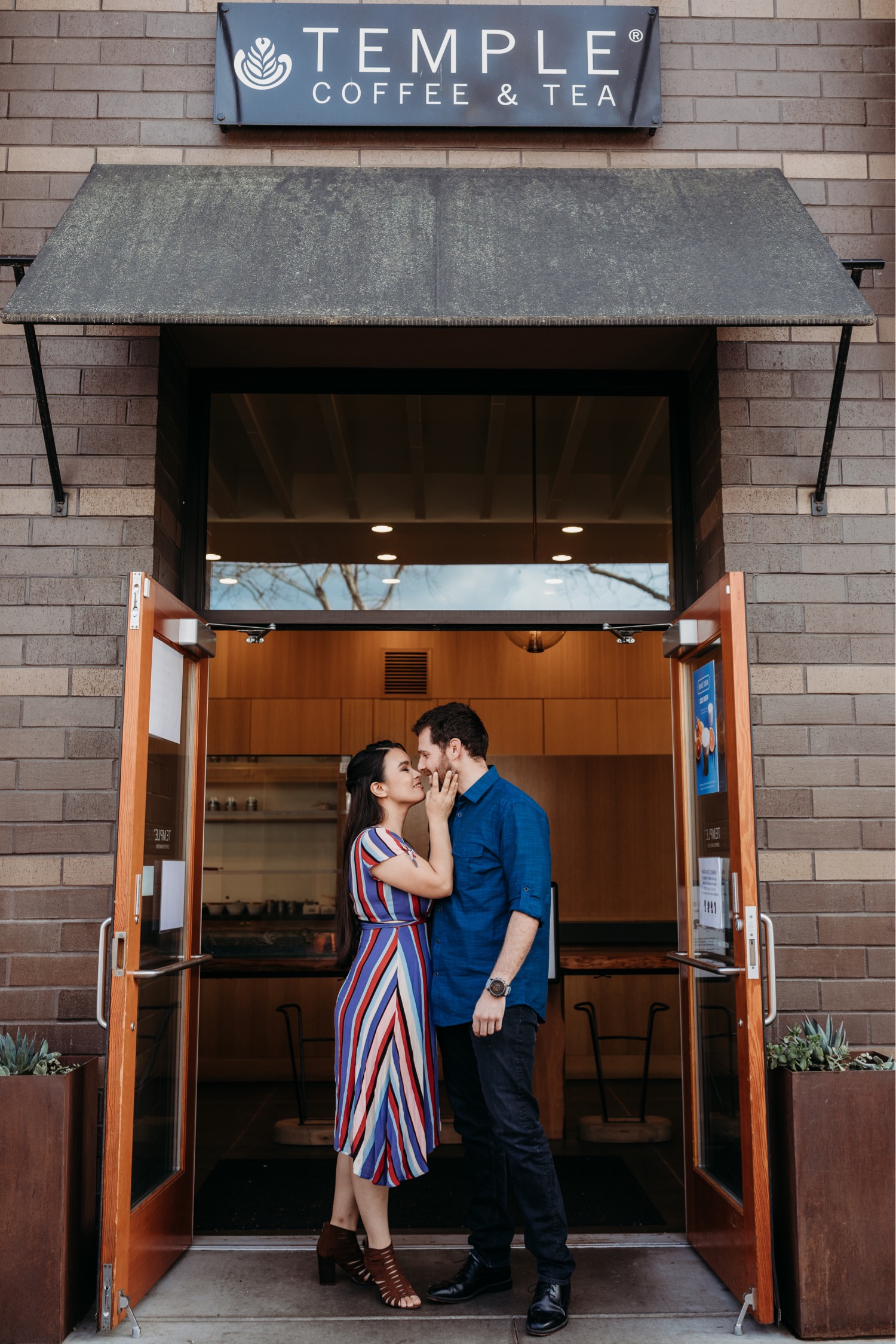 Couple leans in for a kiss at the entrance of the Temple Coffee and Tea shop during their Davis engagement photoshoot.
