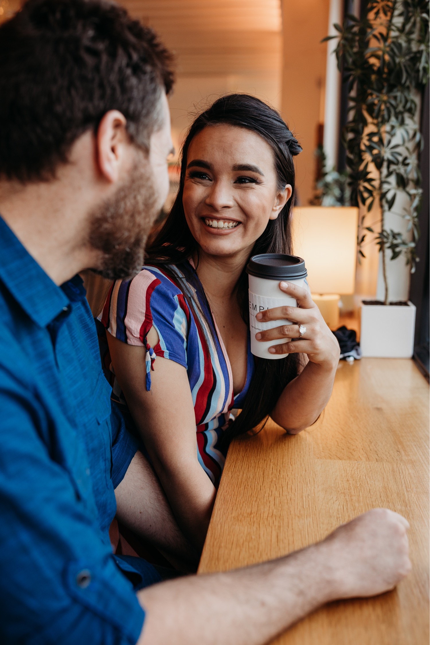 Couple smiles at each other while talking during their coffee shop engagement photos in Davis, CA.