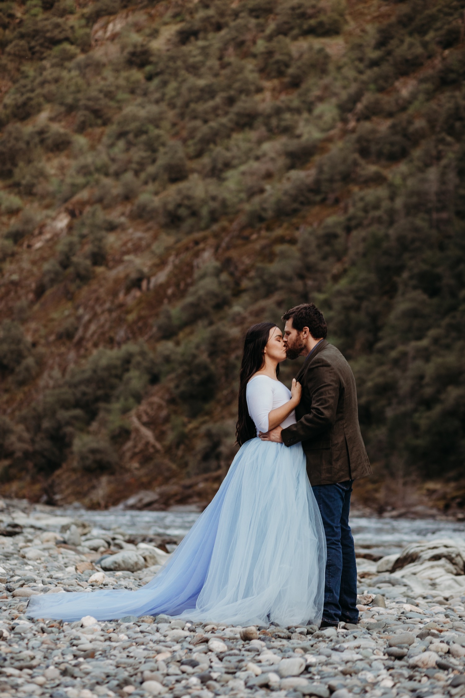 Couple kisses on the rocky short of the American River during their engagement photoshoot.