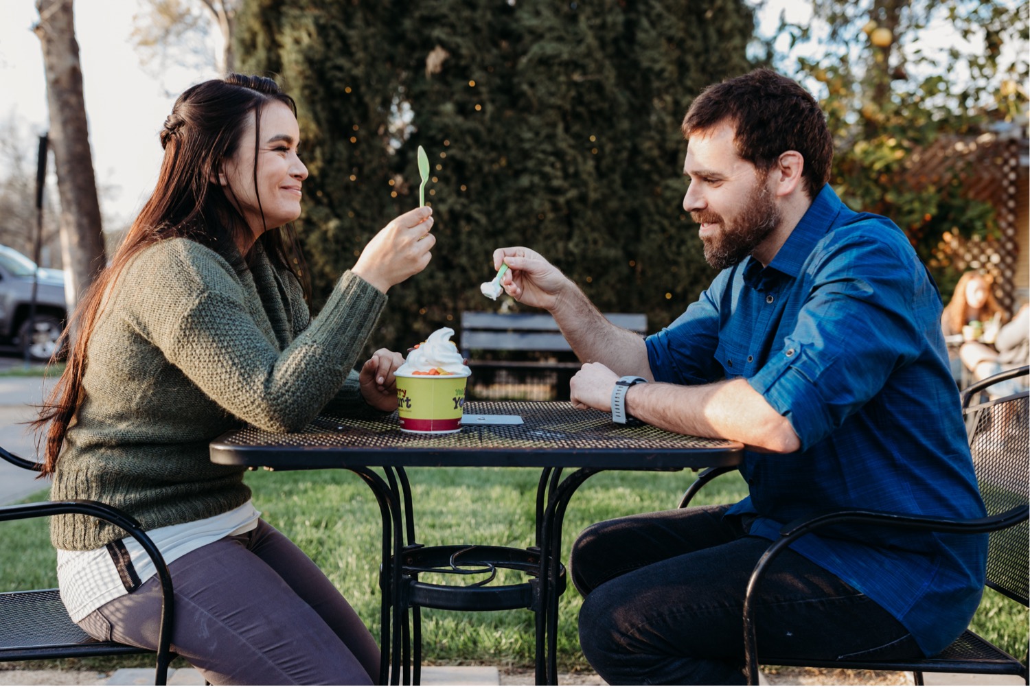 Couple sits at a park table sharing frozen yogurt.