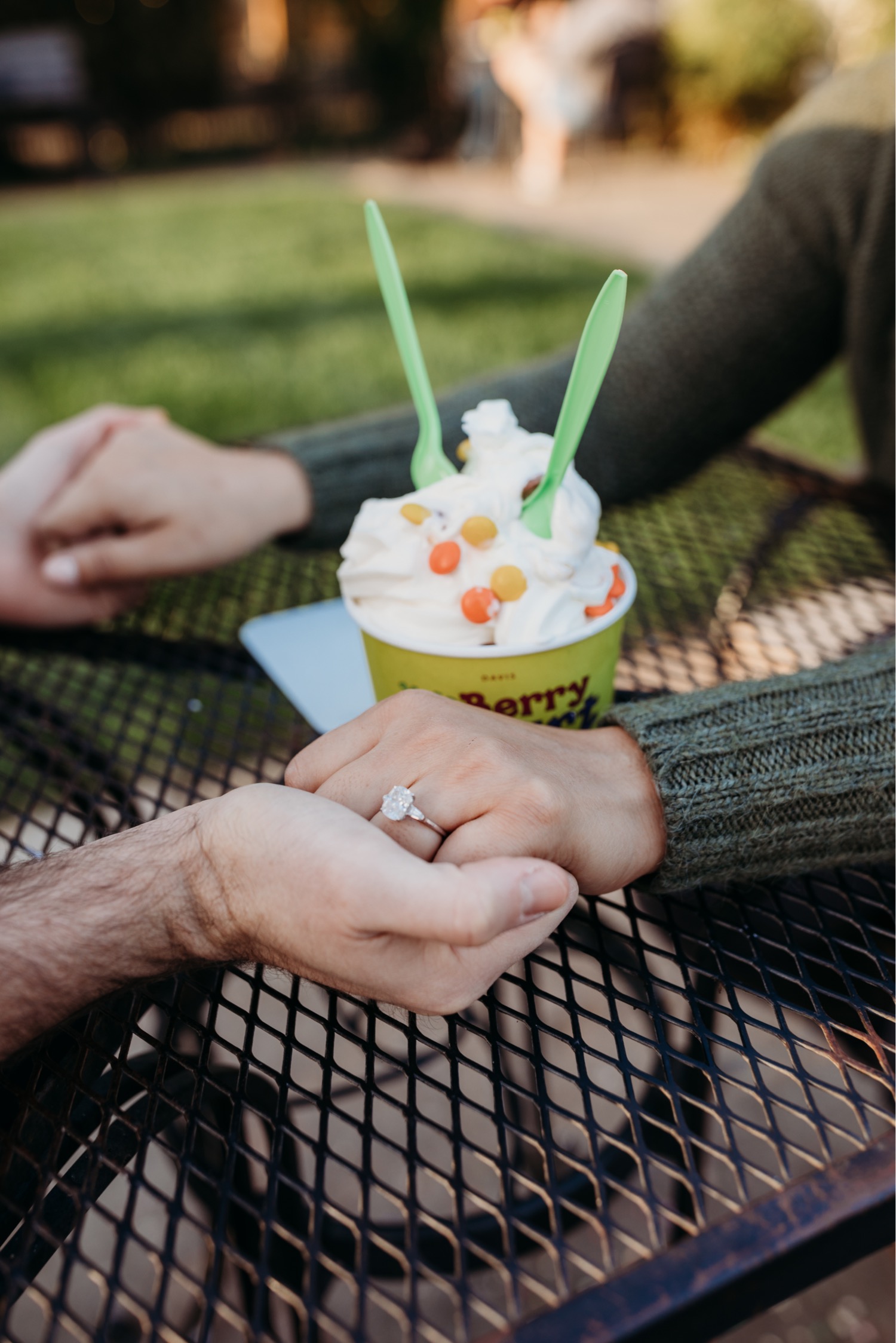 Close up of couple holding hands around a frozen yogurt cup with a close up of her engagement ring.