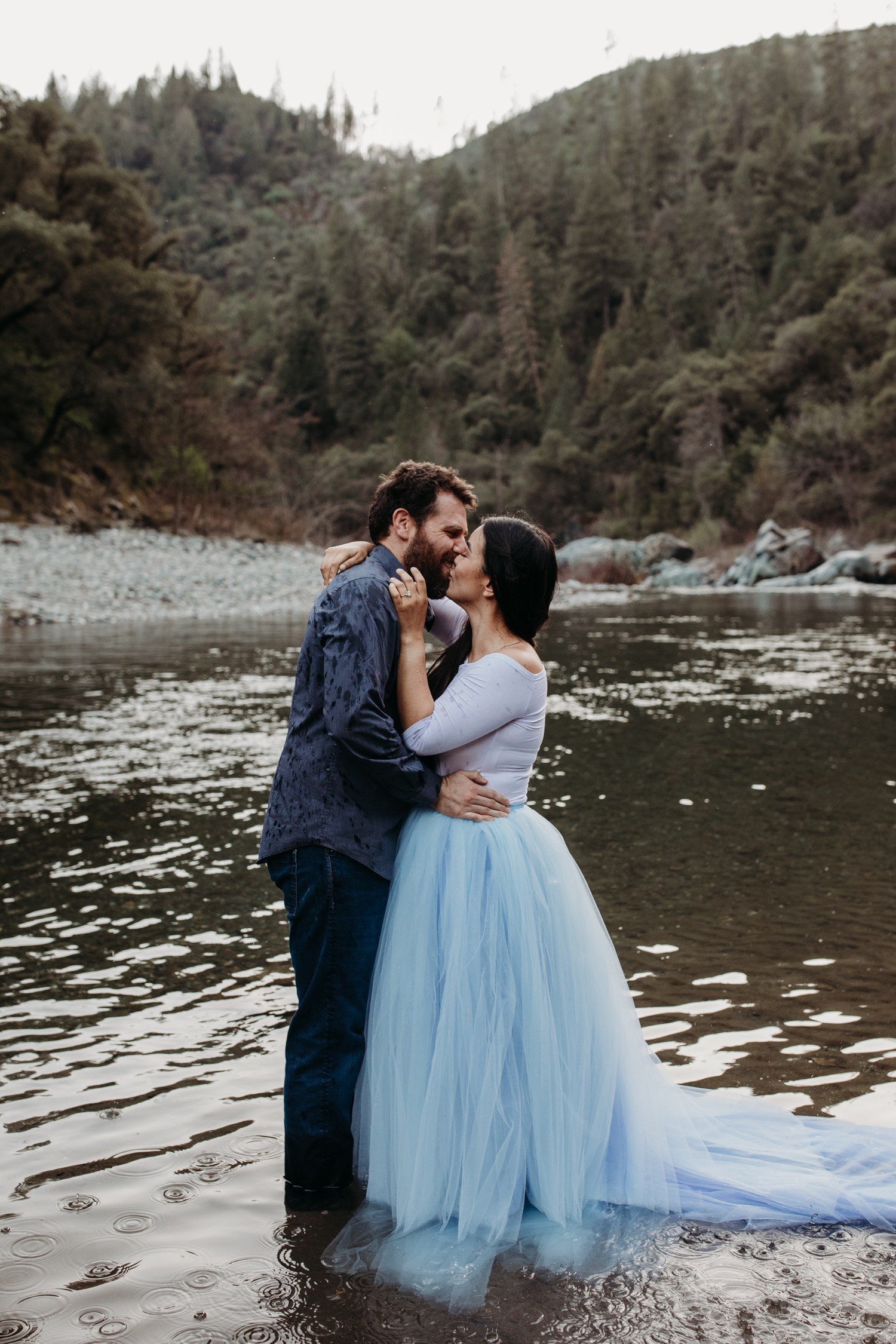 Couple kisses while standing in the American River during their Sacramento engagement photoshoot.