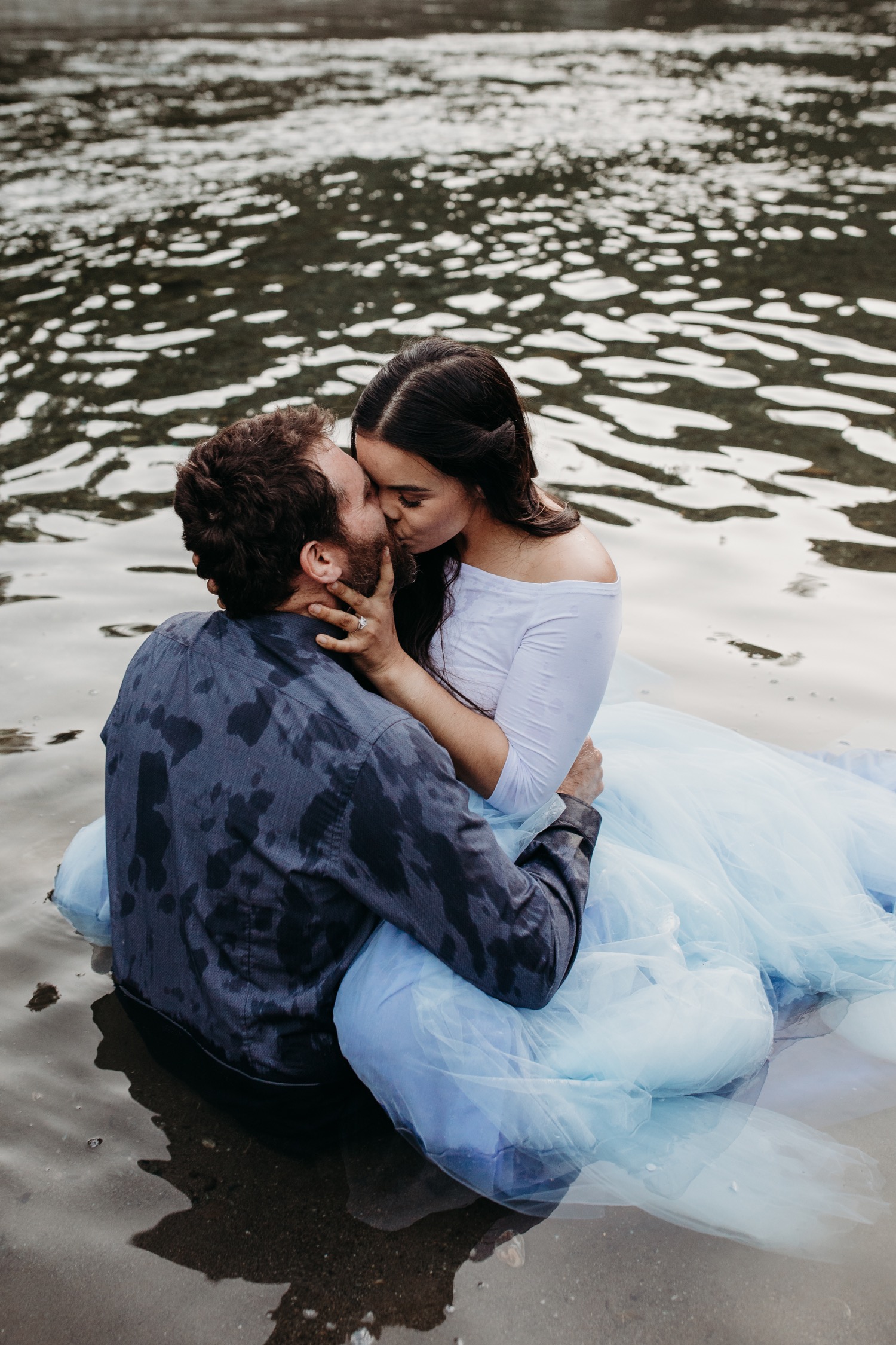 Couple kisses while sitting in the American River during their Sacramento engagement photoshoot.