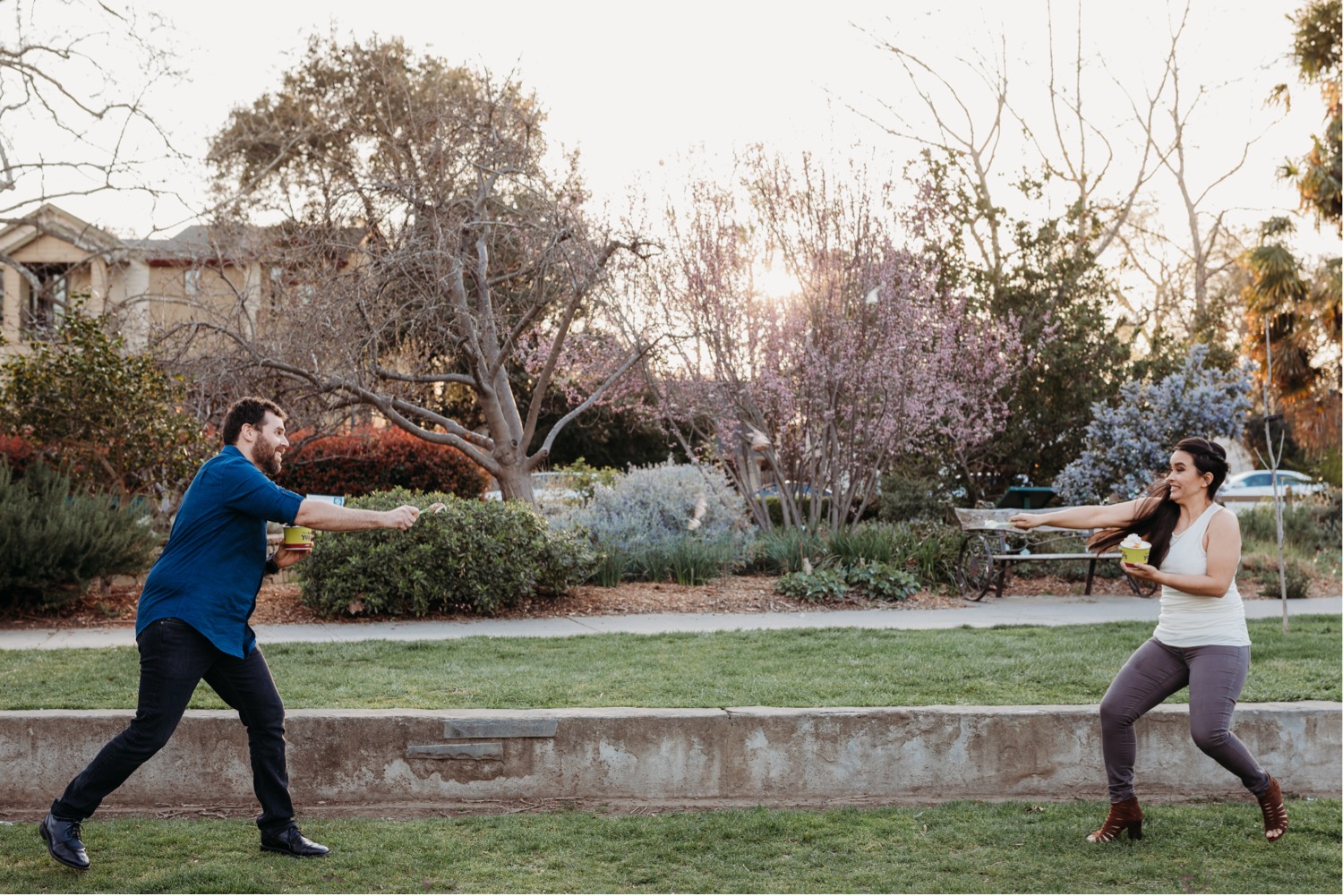 Couple stands far apart and throws frozen yogurt at each other starting an ice cream fight during their engagement photoshoot.