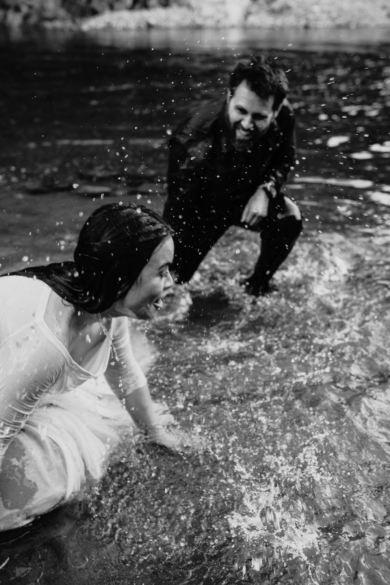 Couple has a water fight in the American River during their engagement photoshoot.