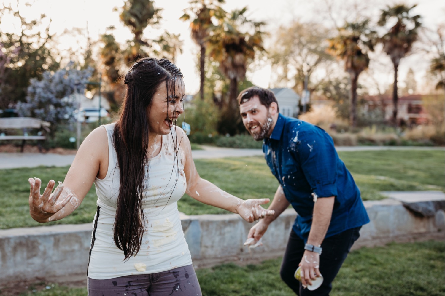 Woman laughs after ice cream food fight with her fiance who is in the background during their Davis engagement photos.
