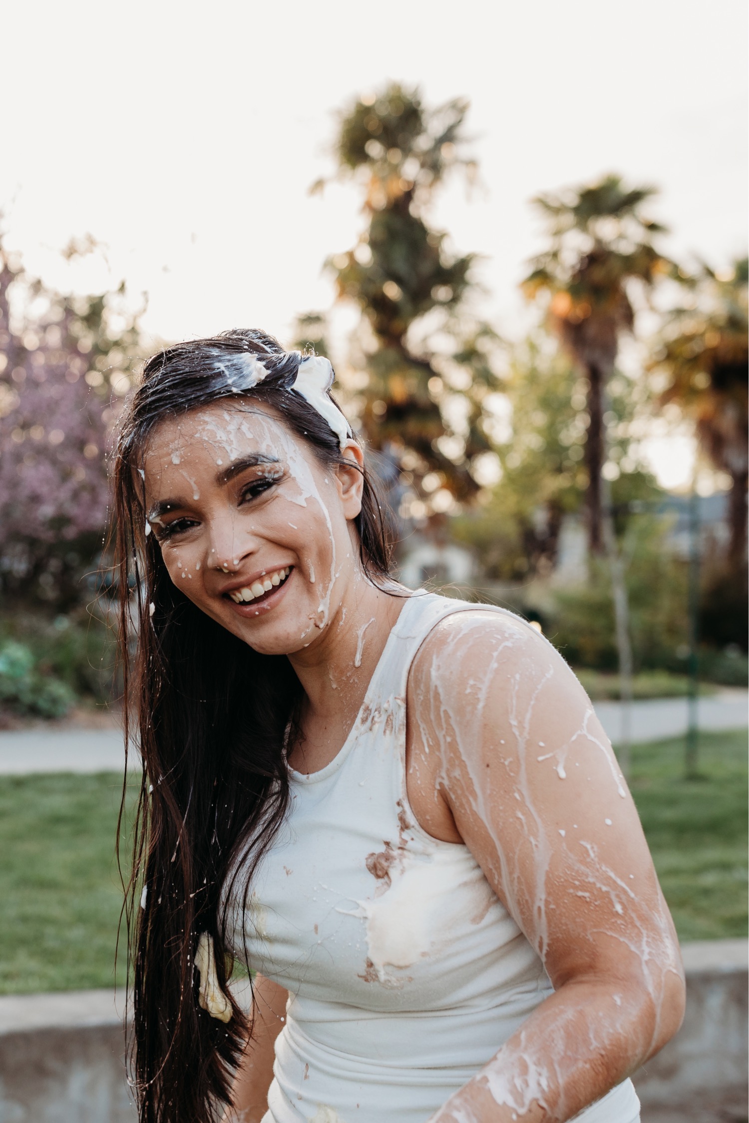 Woman covered in ice cream smiles big at the camera during her engagement photoshoot.