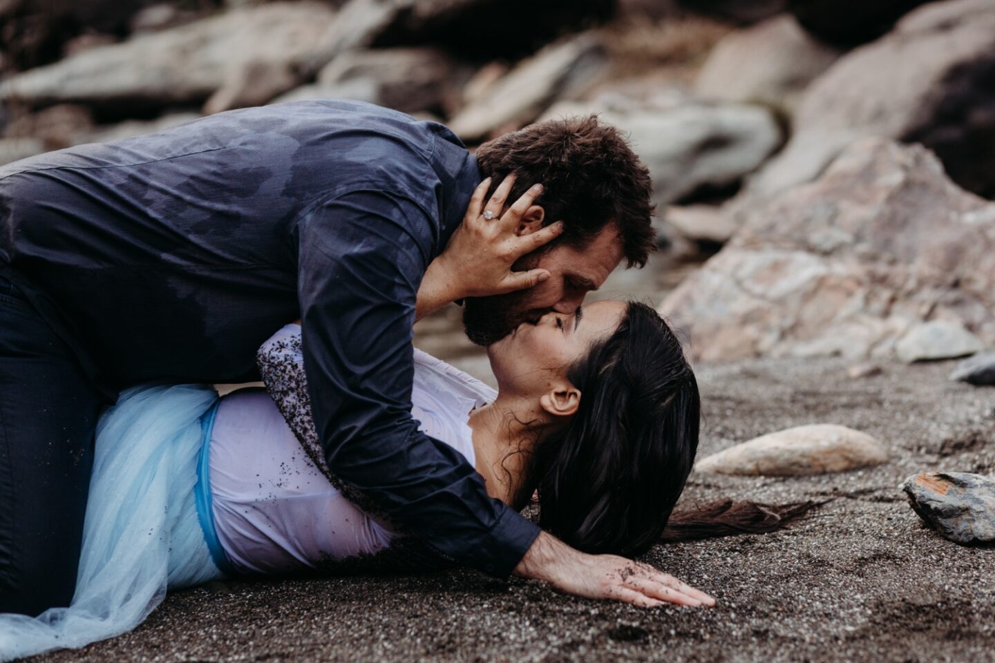 Couple lays on the sand kissing passionately during their American River engagement photoshoot.
