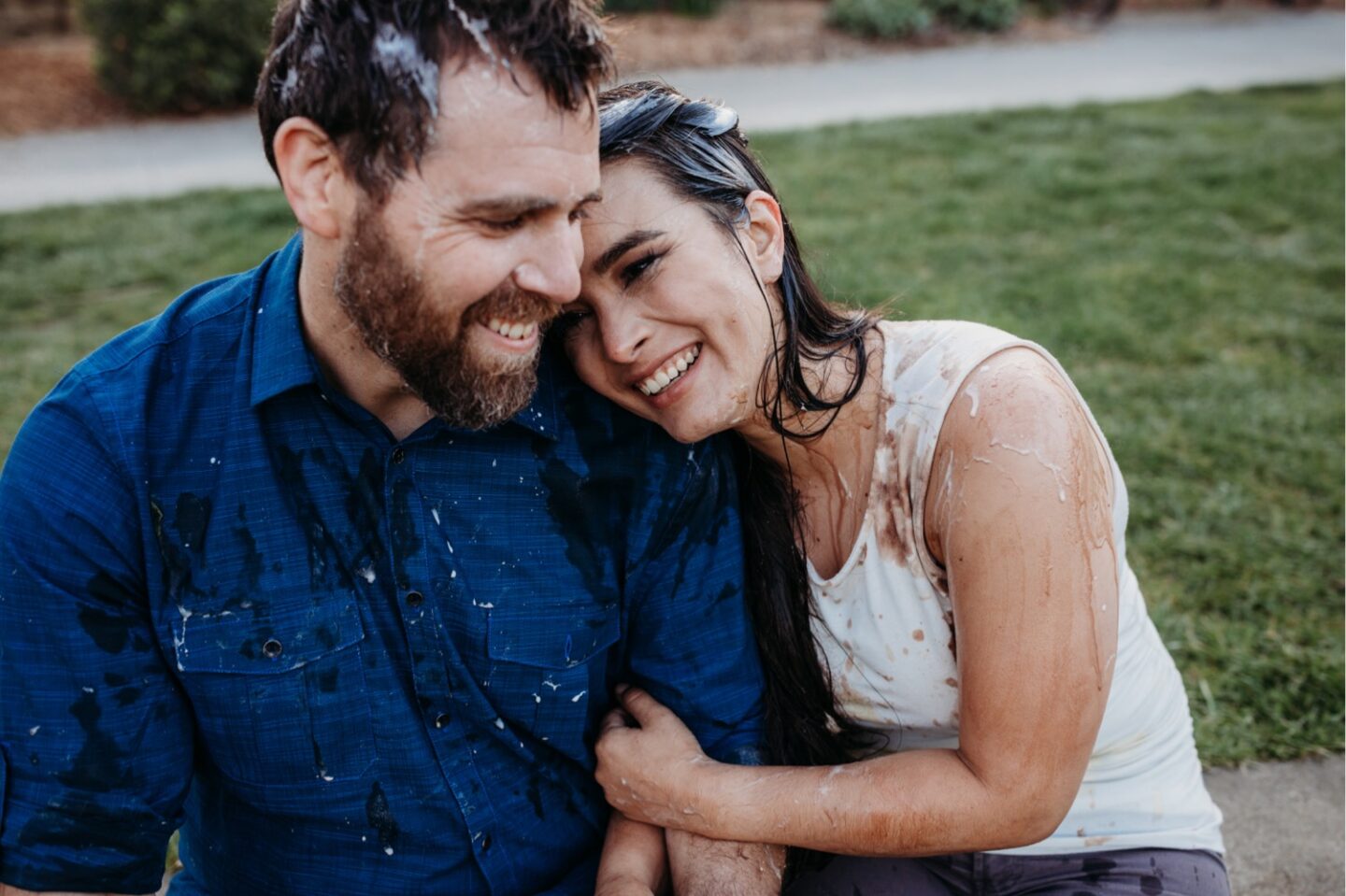 Woman leans her head on her fiance's shoulder as they're both covered in ice cream after their ice cream food fight.