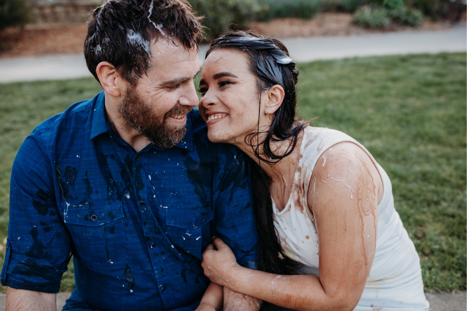 Couple smile wide at each other covered in ice cream after their ice cream food fight during their downtown Davis engagement photos.