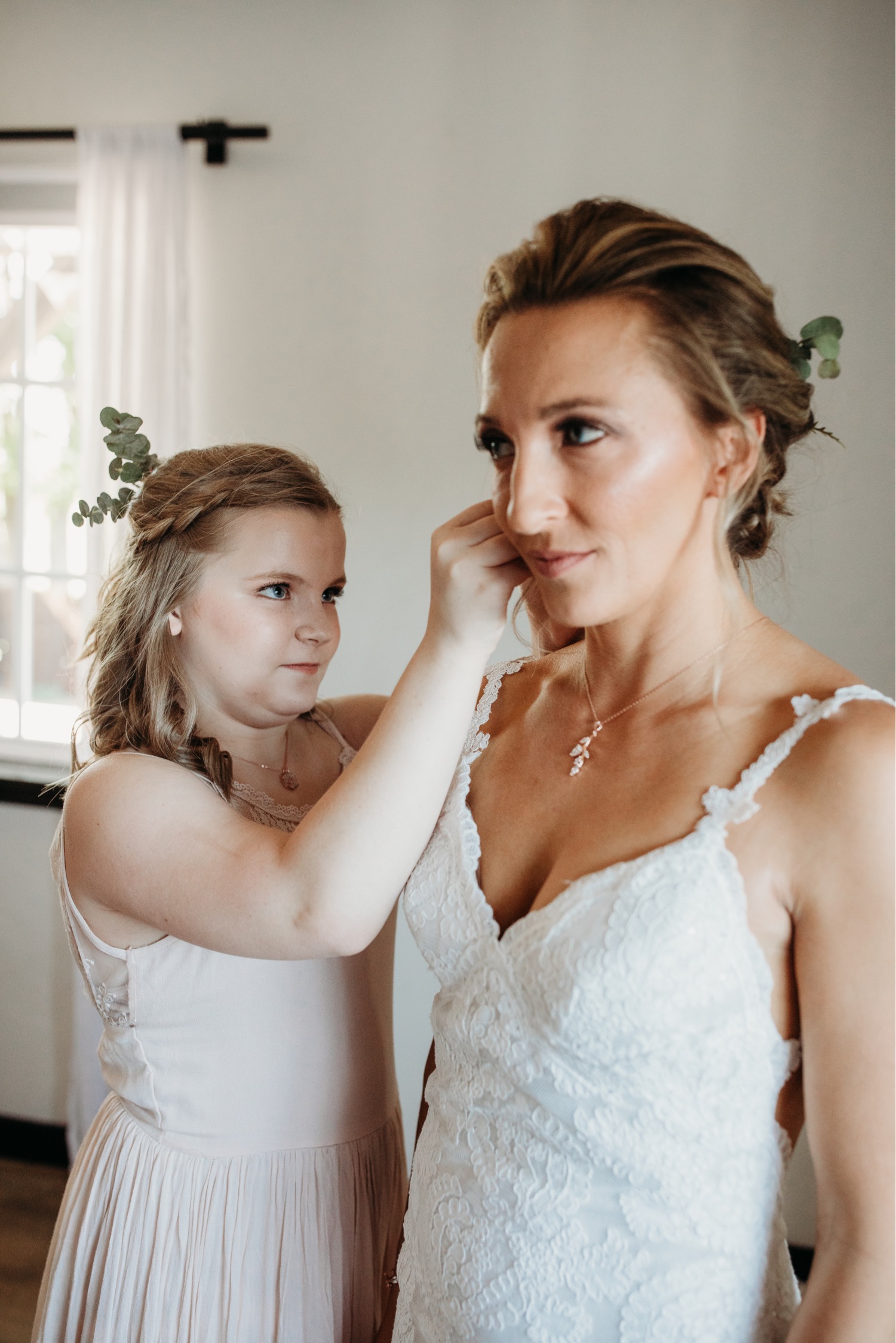 Young bridesmaid helps put the bride's earrings on before her Paso Robles winery wedding. Liz Koston Photography.