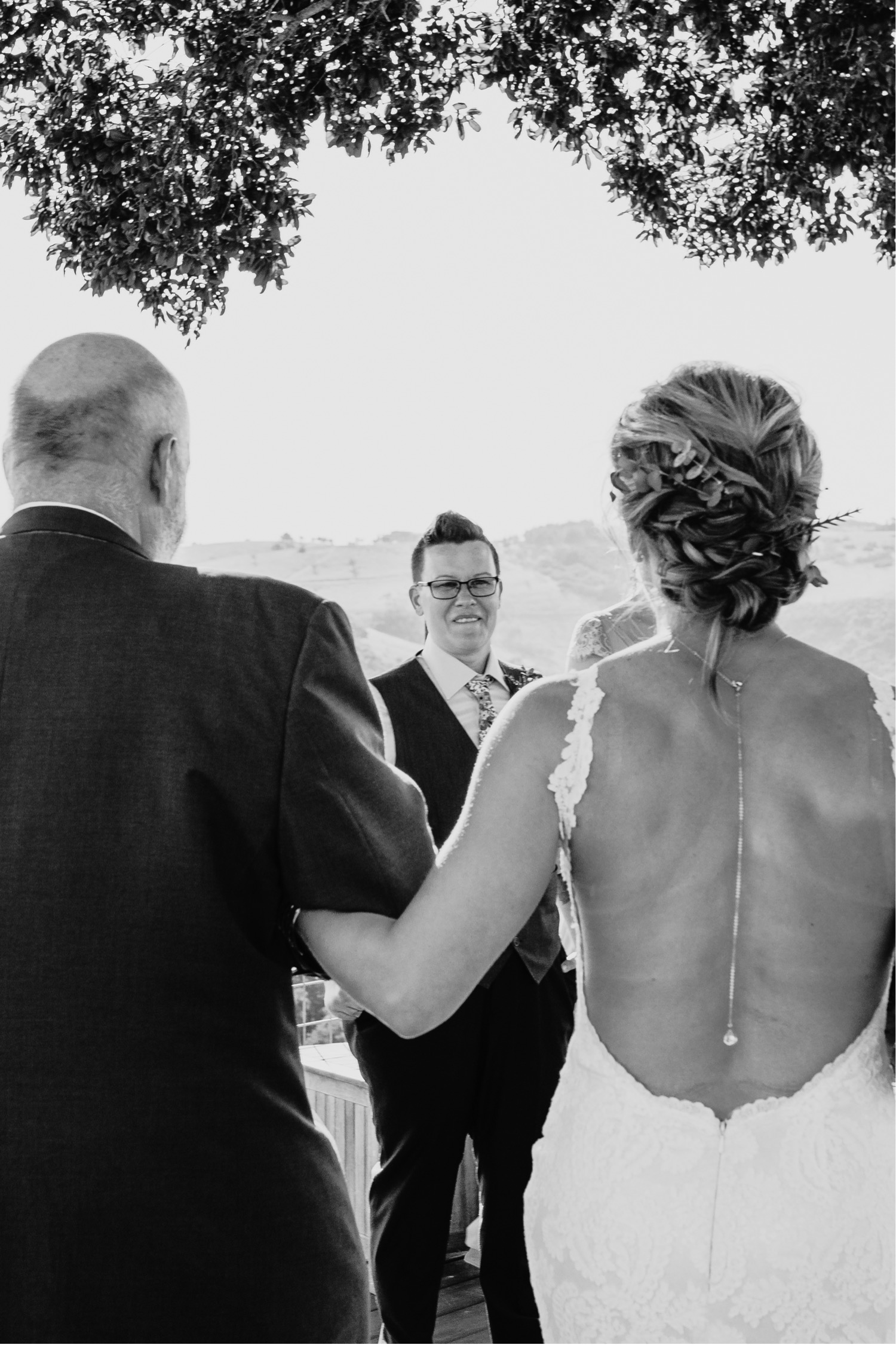 Father of the Bride leads the bride to the other bride as she smiles at them. Liz Koston Photography.