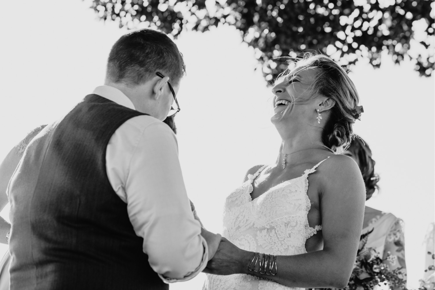 Bride in white lace wedding dress laughs loudly as she exchanges vows. Liz Koston Photography.