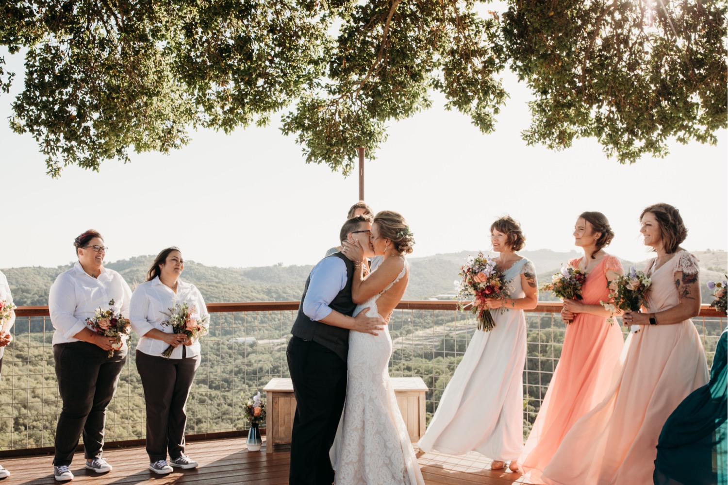 Brides kiss surrounded by friends overlooking the California vineyard. Liz Koston Photography.