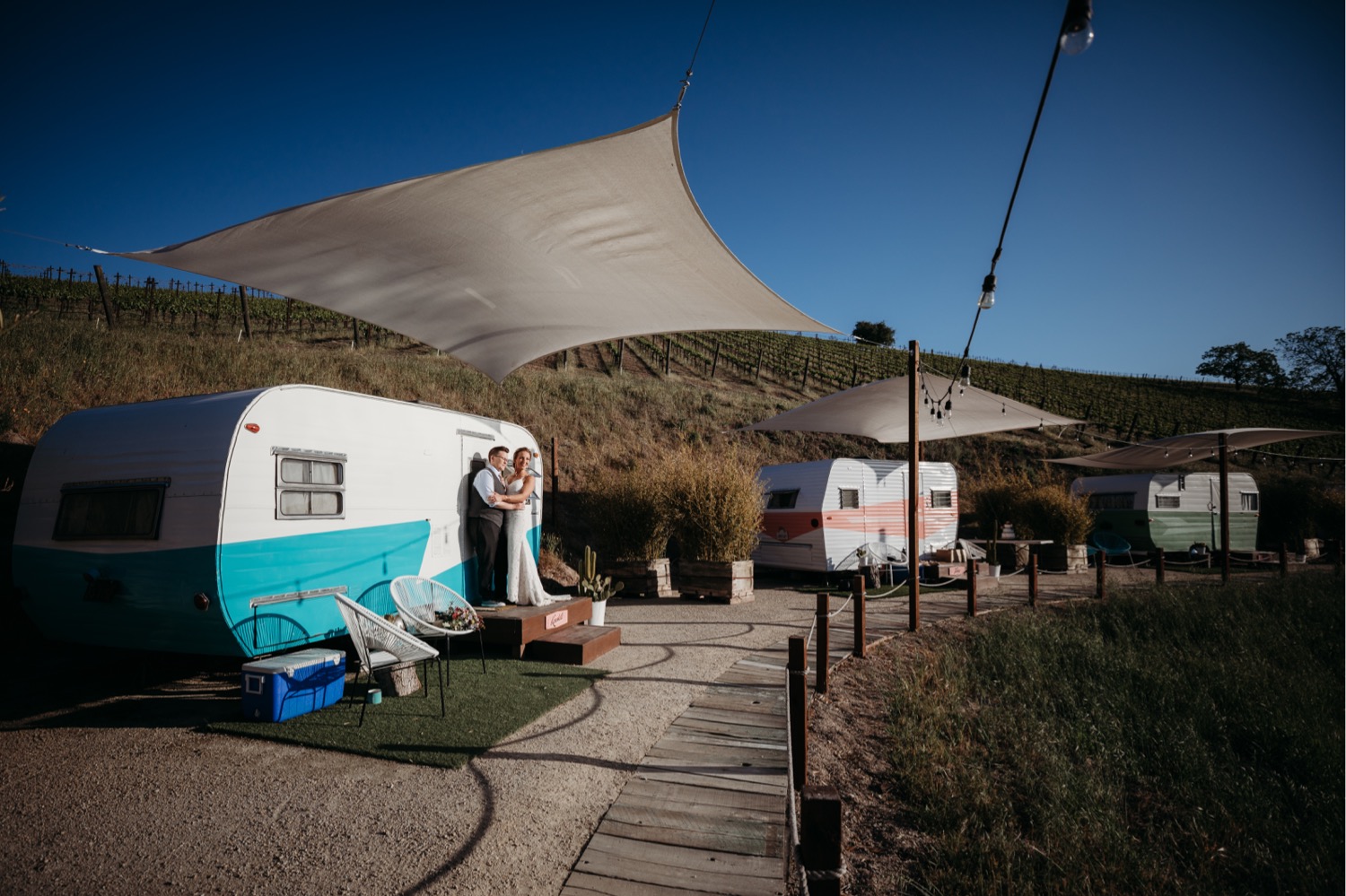 Brides stand in front of a small blue and white trailer at the Alta Colina Trailer Pond. Liz Koston Photography.